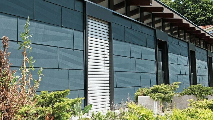 Modern exposed building side designed using FX.12 façade panelling in anthracite, with a garden.