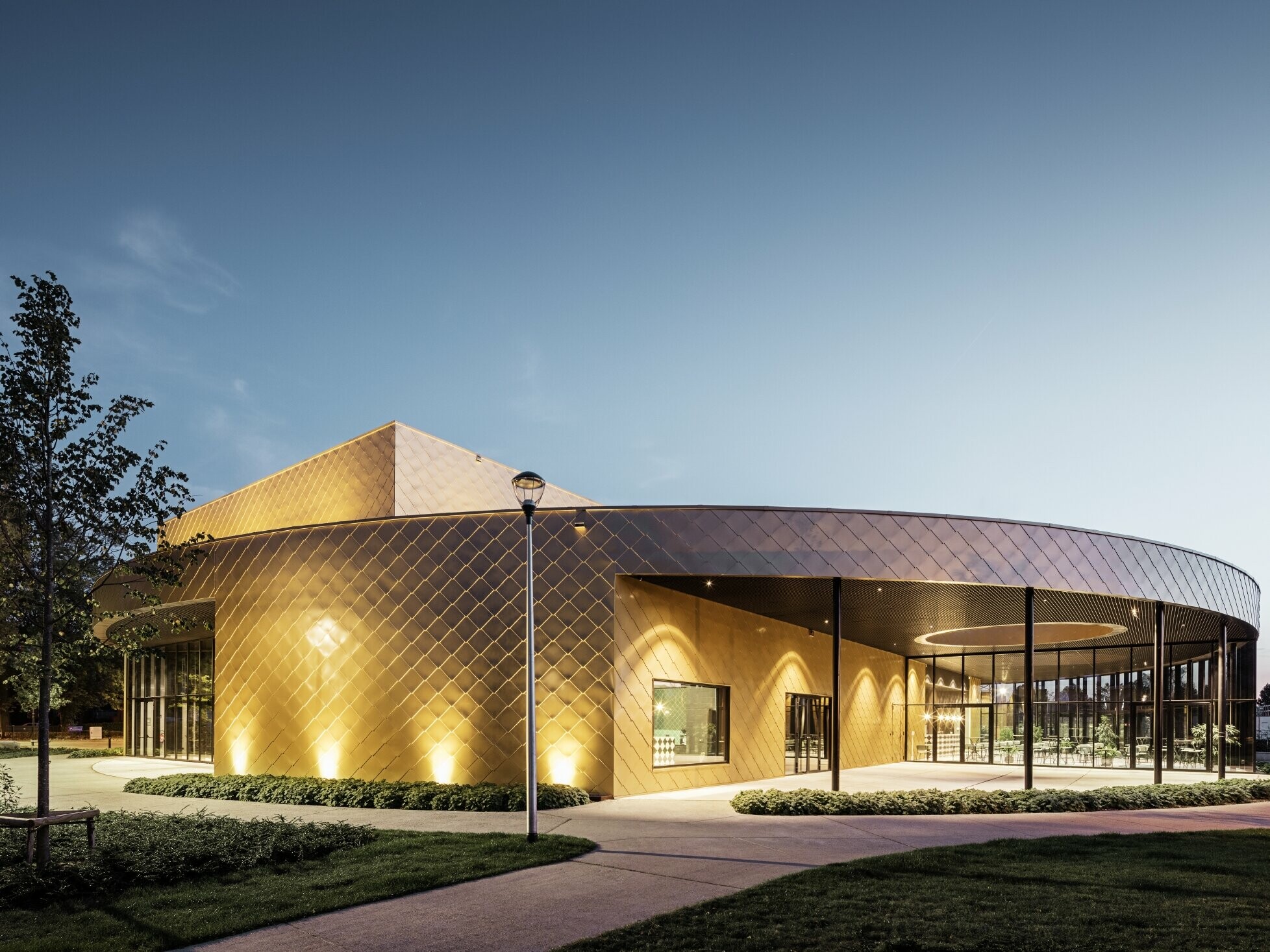 Image of the polyvalent chapels at dusk with PREFA’s rhomboid façade tile 44 × 44 in maya gold