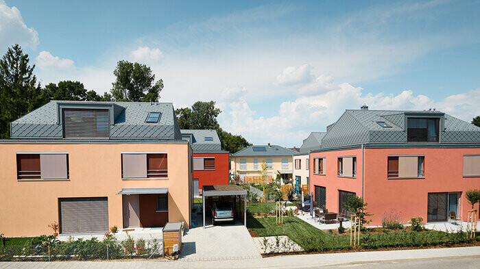 Multi-party housing estate with façades in red tones and aluminium rhomboid roofs in light grey by PREFA