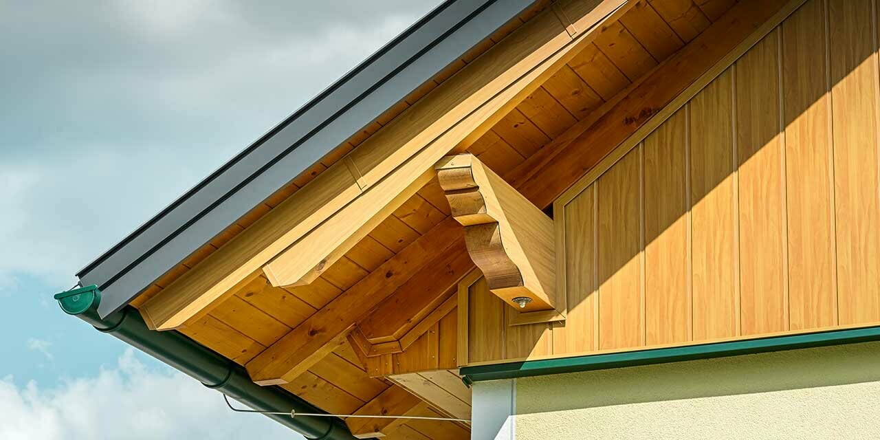 Close-up of gable cladding with PREFA siding in a wood finish with green roof gutter.