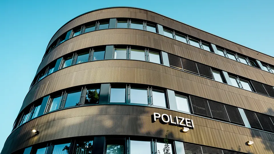Dramatische Untersicht des geschwungenen Neubaus vom Polizeikommissariat 43 in Hamburg: Die markante PREFA Aluminiumfassade aus eloxierten Strangpressprofilen „Zacke“ in Mittelbronze zieht als architektonischer Eyecatcher alle Blicke auf sich. Die feine, rhythmische Struktur erzeugt dynamische Licht- und Schattenverläufe und betont die fließenden Rundungen des Baukörpers. PREFA Aluminium überzeugt durch hohe Witterungsbeständigkeit, Korrosionsschutz und Langlebigkeit – eine nachhaltige, wartungsarme Lösung für präzise, moderne Fassadenarchitektur.