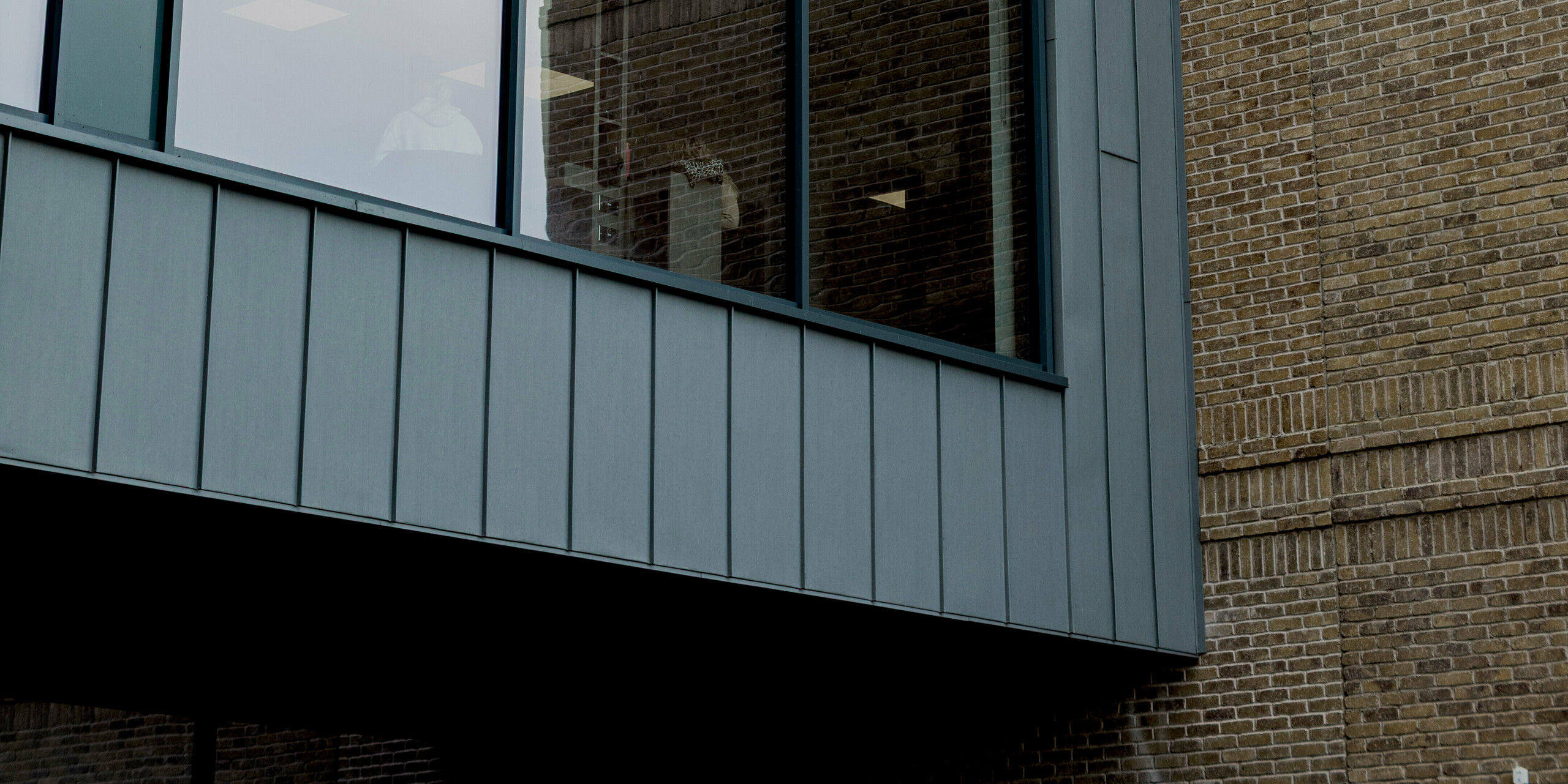 A striking façade detail of the Northern Regional College in Ballymena highlights a large glazed section precisely framed by PREFALZ standing seam cladding in patina grey. The vertical rhythm of the aluminium cladding accentuates the sharp geometry of the cantilevered volume, while contrasting with the textured brickwork behind. The refined metal surface enhances the building’s modern character. PREFA aluminium provides durability, weather resistance and a clean, low-maintenance solution for contemporary educational architecture.
