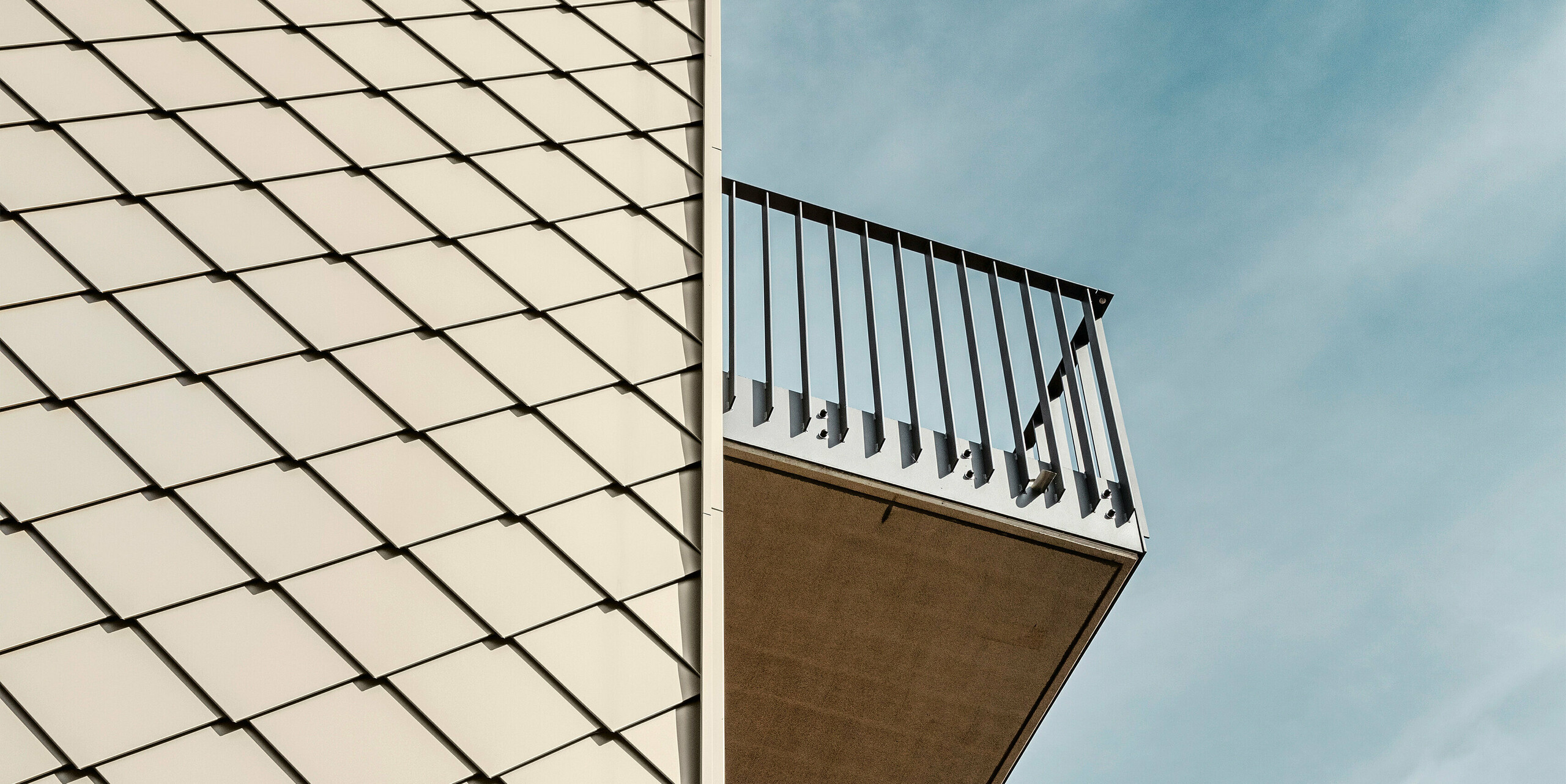 Nahaufnahme der Fassade eines modernen Mehrfamilienhauses in Dresden mit präzise angeordneten PREFA Wandrauten 29 × 29 in Bronze. Das Bild zeigt die klare Struktur der hochwertigen Aluminiumfassade sowie die Balkone mit ihren minimalistischen Geländern, die in Kontrast zur bronzefarbenen Oberfläche stehen. Die Kombination von Materialien und Formen unterstreicht die elegante Architektur des Gebäudes.