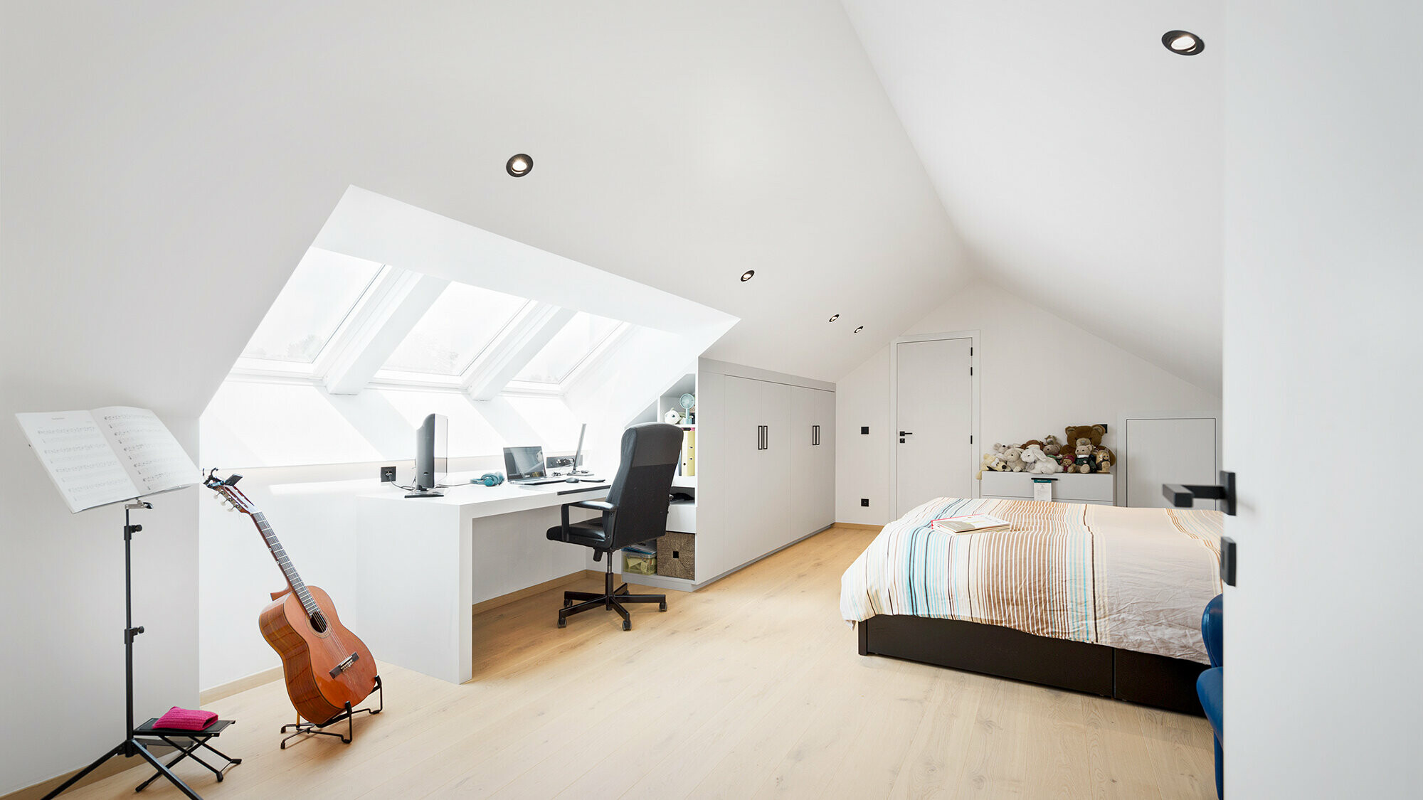 Interior view of one of the light rooms in the attic with a bed, desk, guitar and music stand.