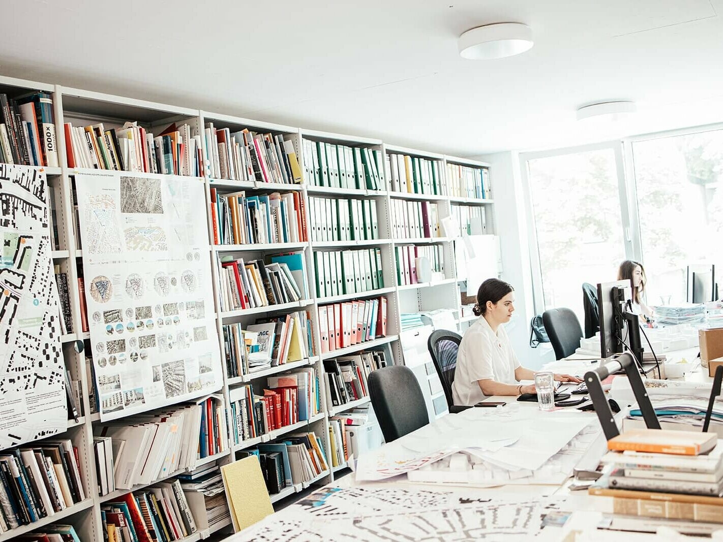 You can see an office, where two empolyees are sitting in front of their computers. In the back there is a bookcase.