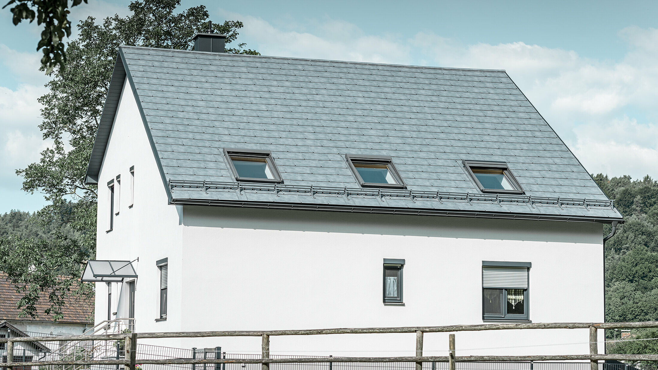 The gabled roof of the classic detached house was covered with the new PREFA R.16 roof tile in stone grey. Three roof windows were inserted in the roof area and snow guards were installed. The façade is kept simple in white.