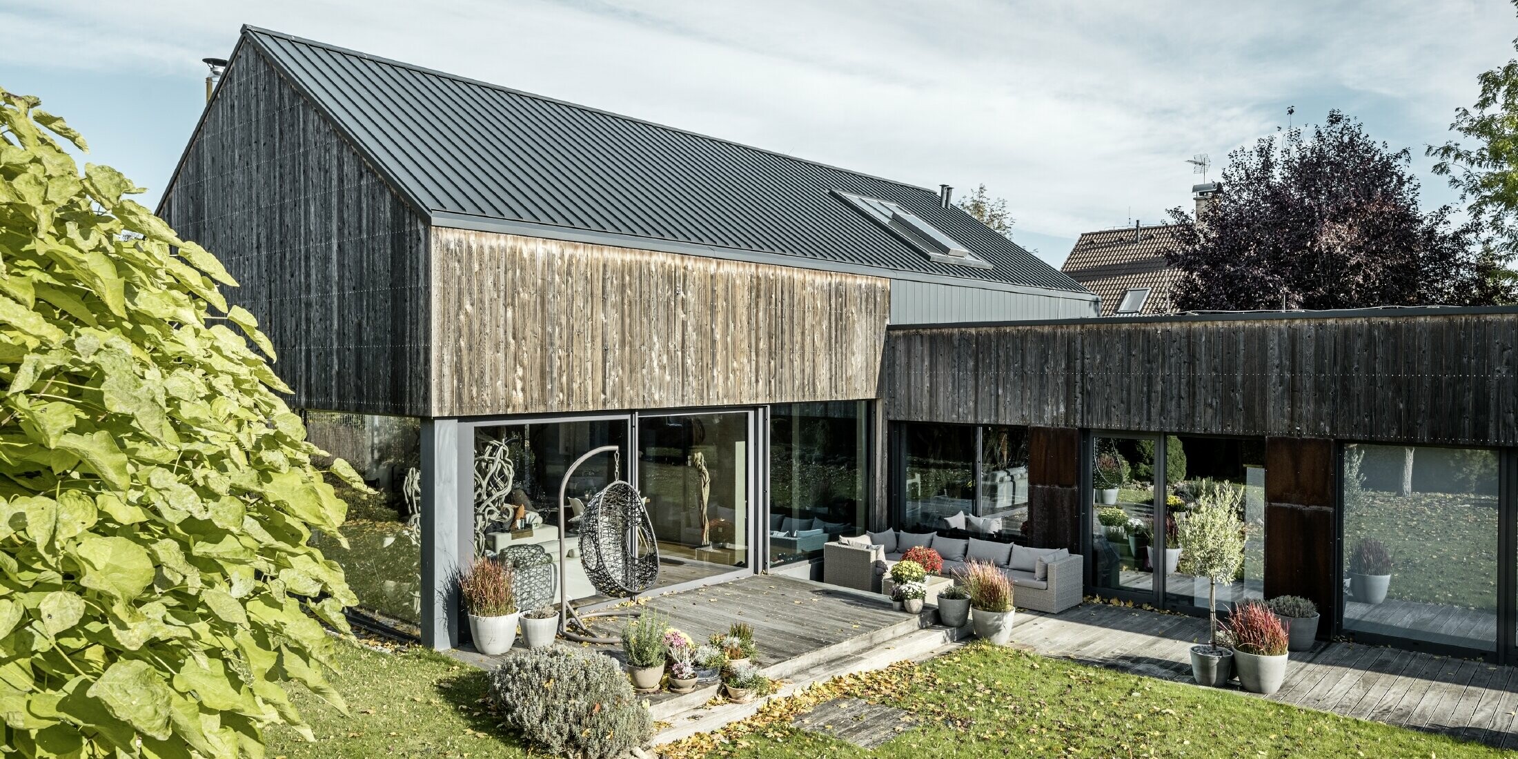 Detached house with gable roof, covered with PREFALZ double standing seam in anthracite and weathered wooden façade. With a beautiful wooden terrace and large windows on the ground floor.