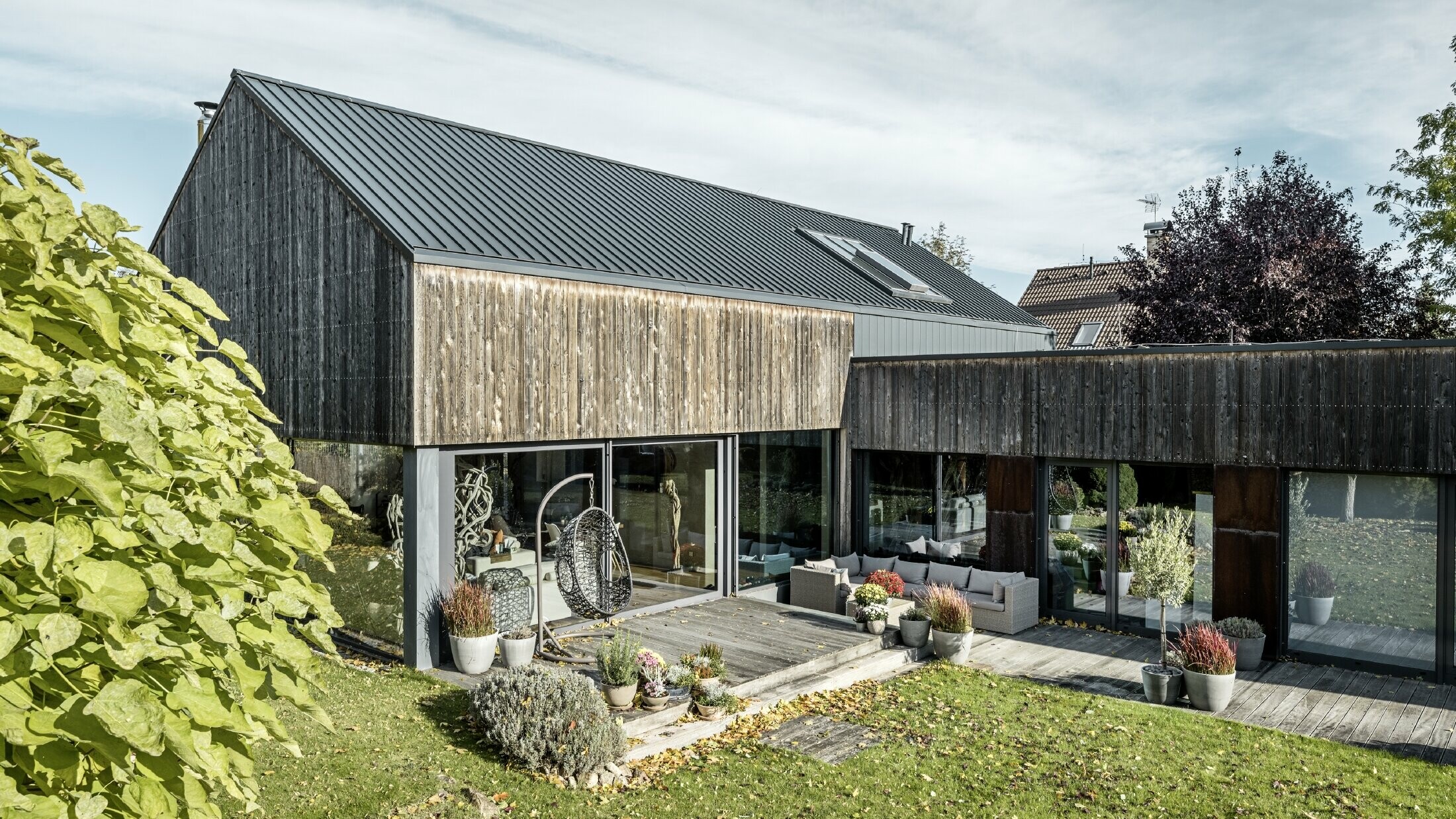 Detached house with gable roof, covered with PREFALZ double standing seam in anthracite and weathered wooden façade. With a beautiful wooden terrace and large windows on the ground floor.