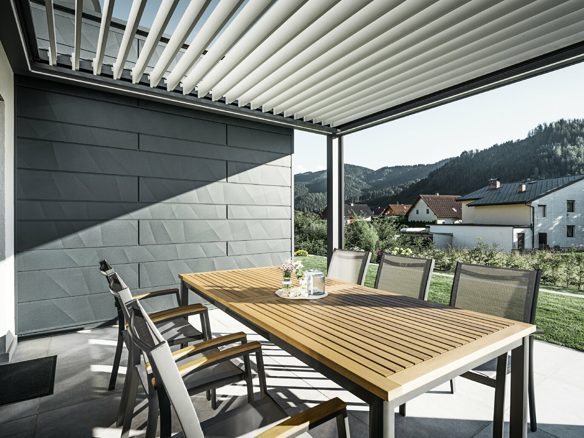 Sheltered terrace covered with slats, with table and chairs; one side of the façade is clad with PREFA Siding.X façade panels in anthracite.