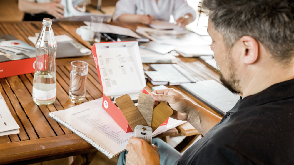 An expert looks at the colour fan. Three samples of the three colours in wood look can be seen: beige grey oak, walnut brown and natural oak.