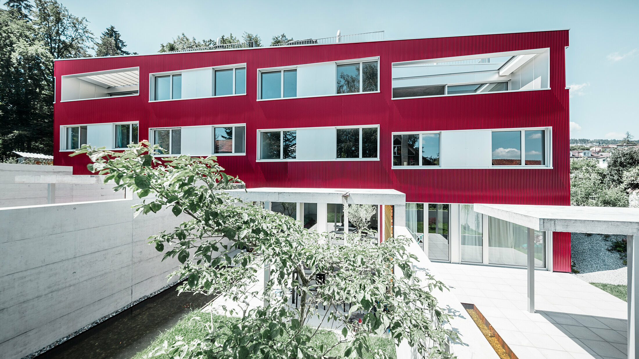 Apartment complex with flat roof and balconies with burgundy façade with PREFA ripple profile 