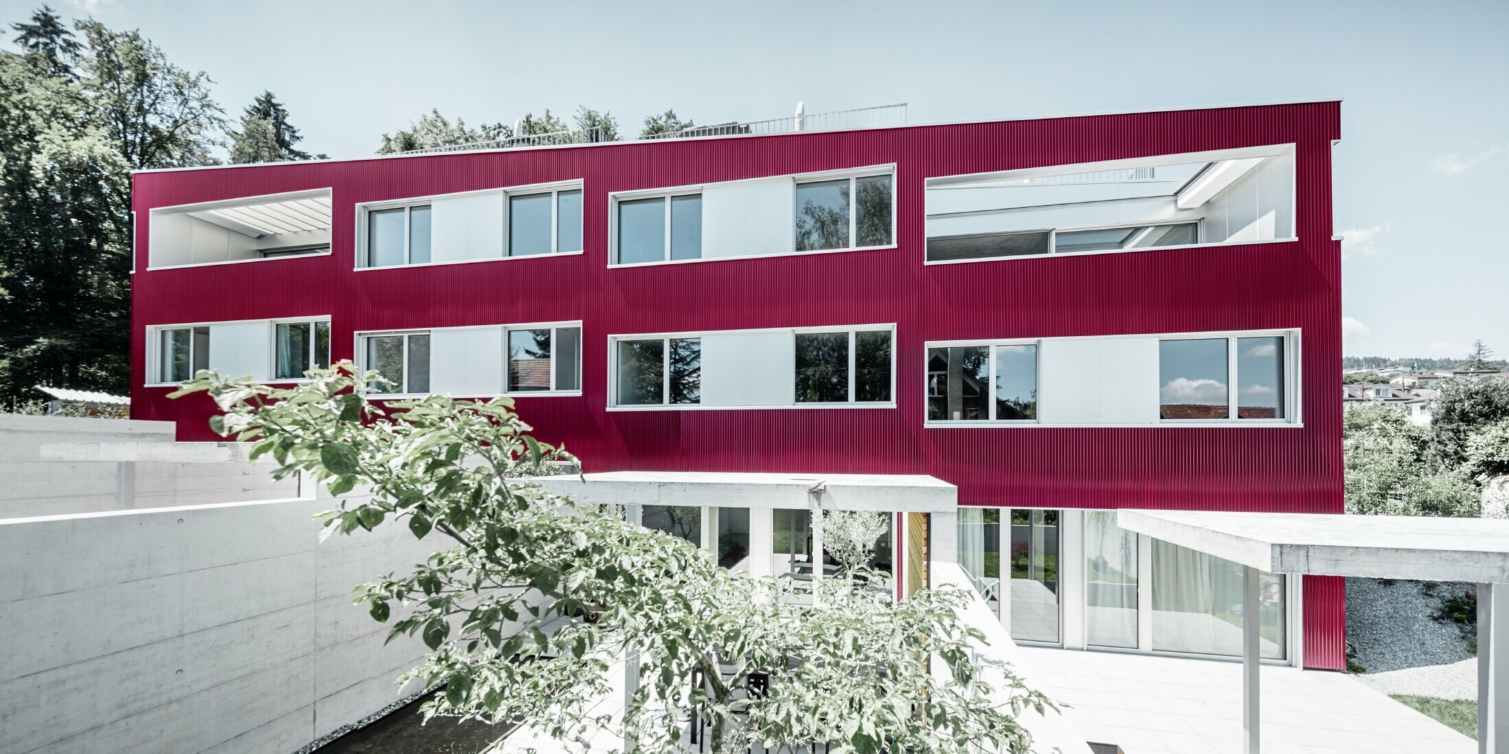 Apartment complex with flat roof and balconies with burgundy façade with PREFA ripple profile 