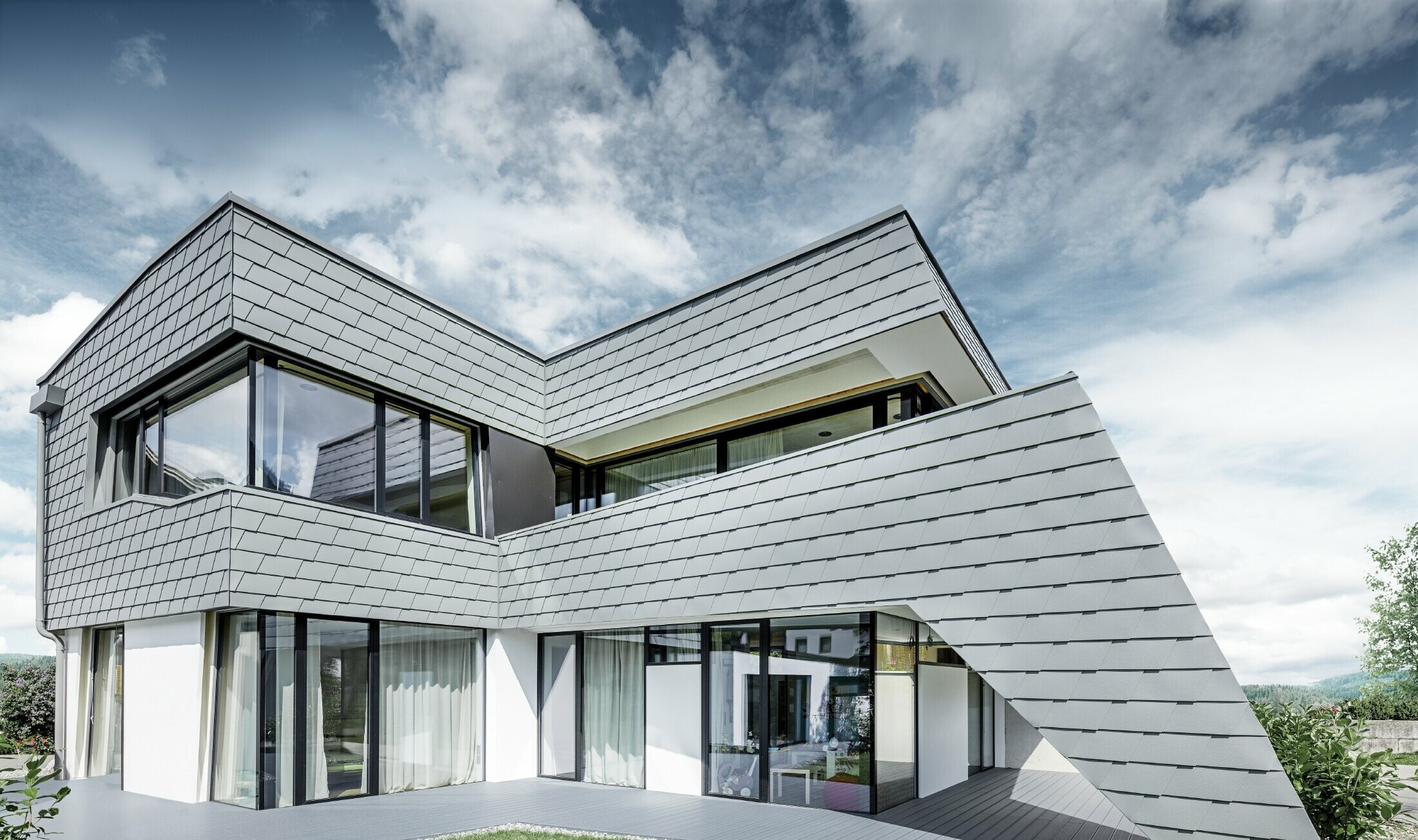 Modern detached house with a flat roof, large windows and a shingle façade in light grey, made of aluminium by PREFA