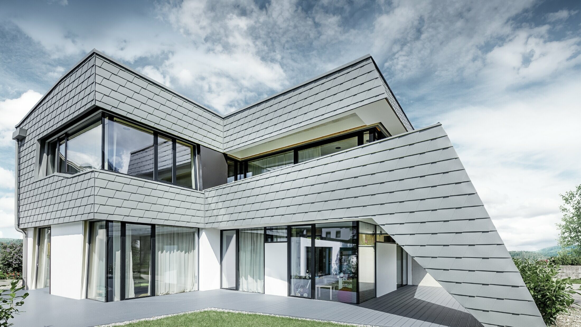 Modern detached house with a flat roof, large windows and a shingle façade in light grey, made of aluminium by PREFA