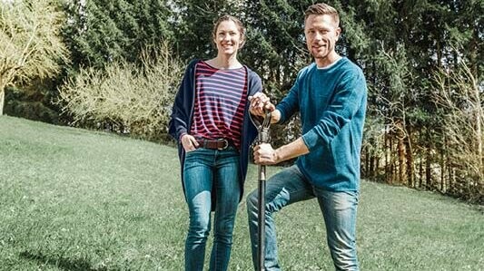 Couple standing on a green lawn, on their building plot, shortly before breaking ground. Here you will find valuable tips and tricks about building!