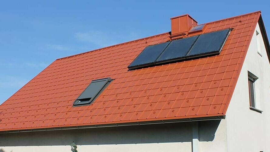 Detached house with gable roof covered with PREFA roof tiles in brick red. Roof includes solar panels and skylight