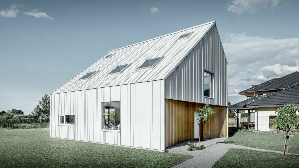 Modern detached house with gable roof, the entire outer skin is clad with PREFALZ in PREFA white. The panels of different widths extend from the roof over the façade. Several roof windows are installed in the roof.