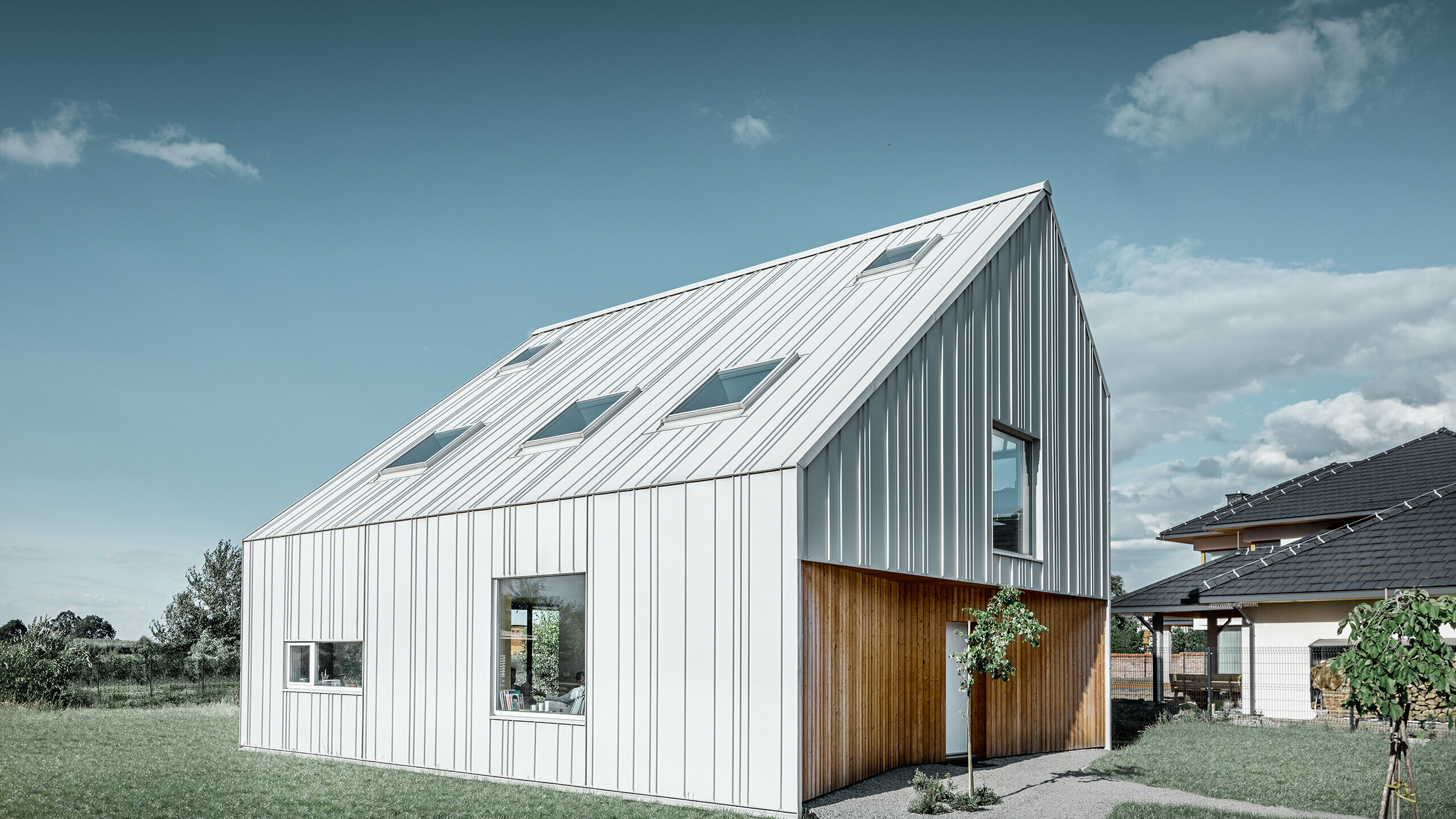 Modern detached house with gable roof, the entire outer skin is clad with PREFALZ in PREFA white. The panels of different widths extend from the roof over the façade. Several roof windows are installed in the roof.