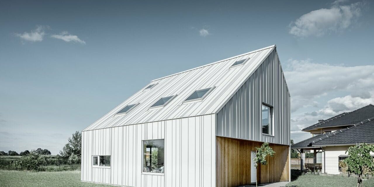 Modern detached house with gable roof, the entire outer skin is clad with PREFALZ in PREFA white. The panels of different widths extend from the roof over the façade. Several roof windows are installed in the roof.