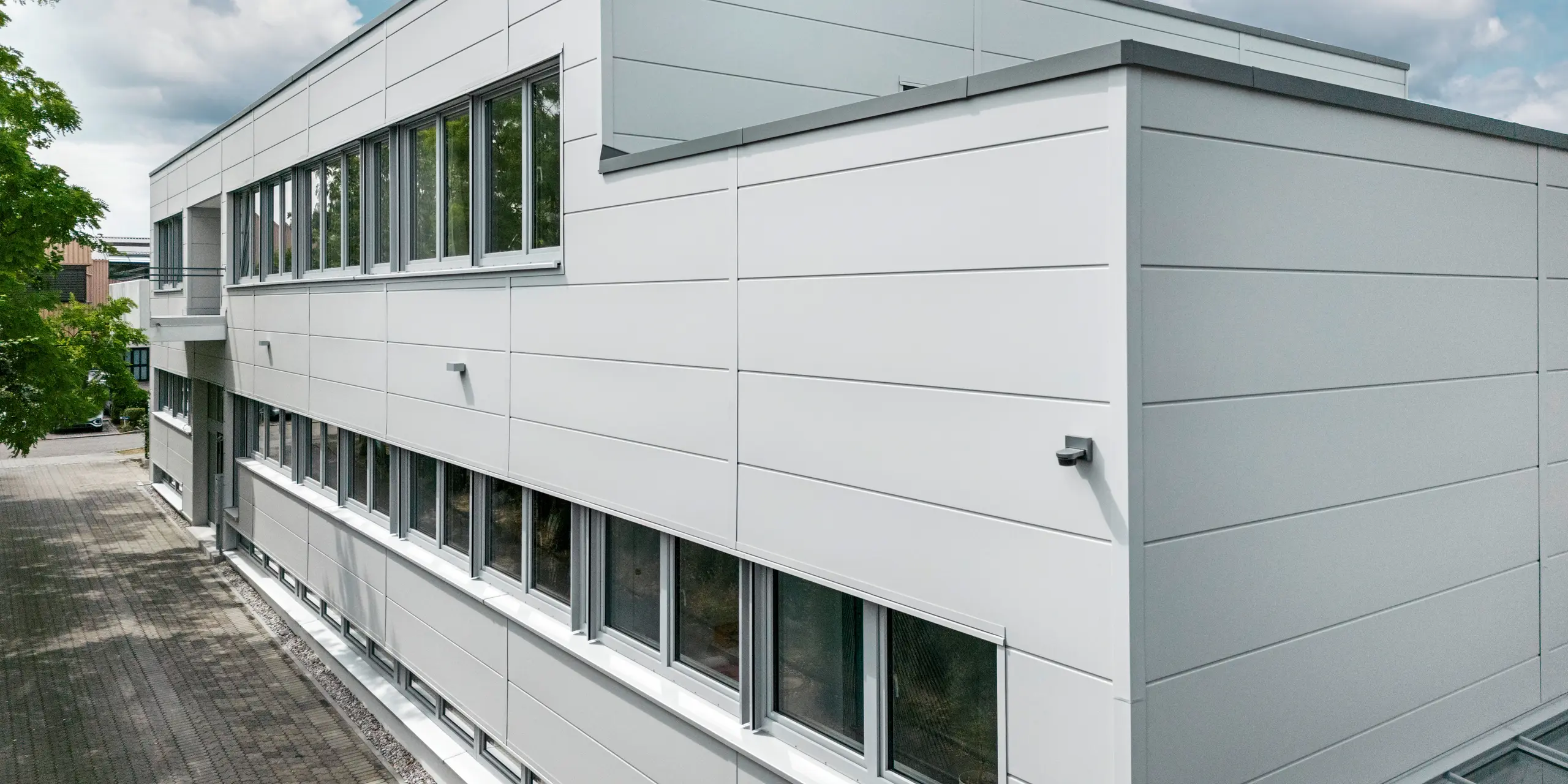 Großformatige PREFA Sidings umhüllen ein Firmengebäude in Oberschleißheim (Deutschland). Die extrabreiten Fassadenelemente aus Aluminium sind in der Farbe Prefaweiß gehalten.