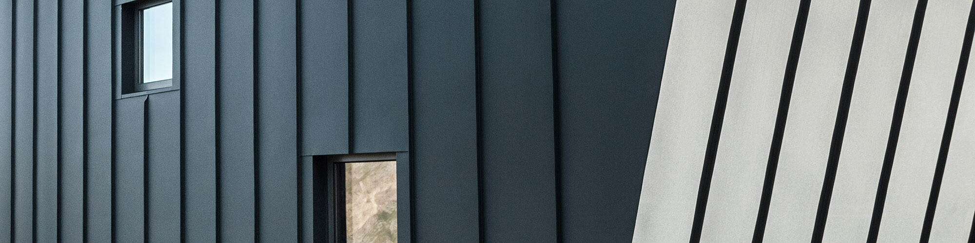Close-up of the façade with two small windows: One side of the façade is illuminated by the sun, the other one appears to have a darker hue in the shade.