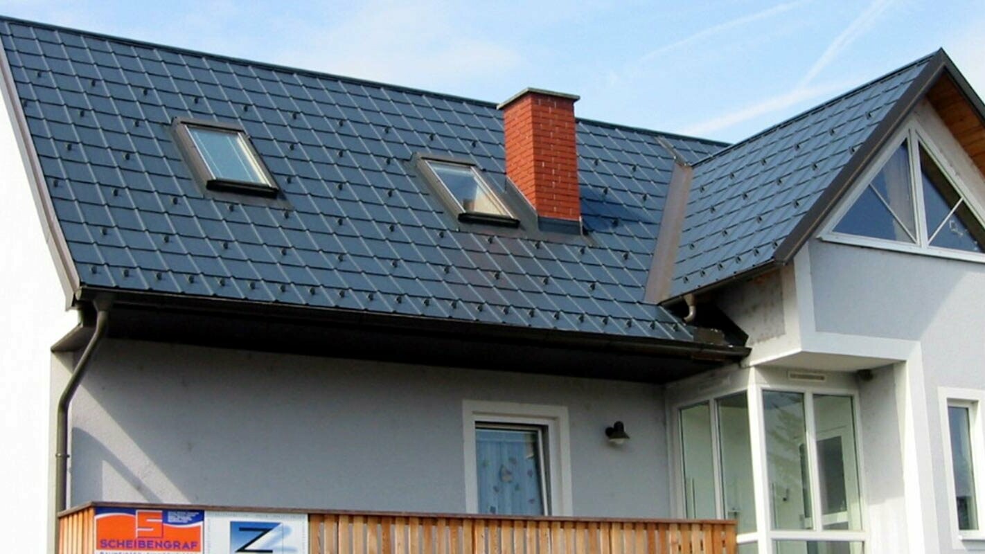 Detached house with a gable roof and a blue façade with a newly renovated roof from PREFA