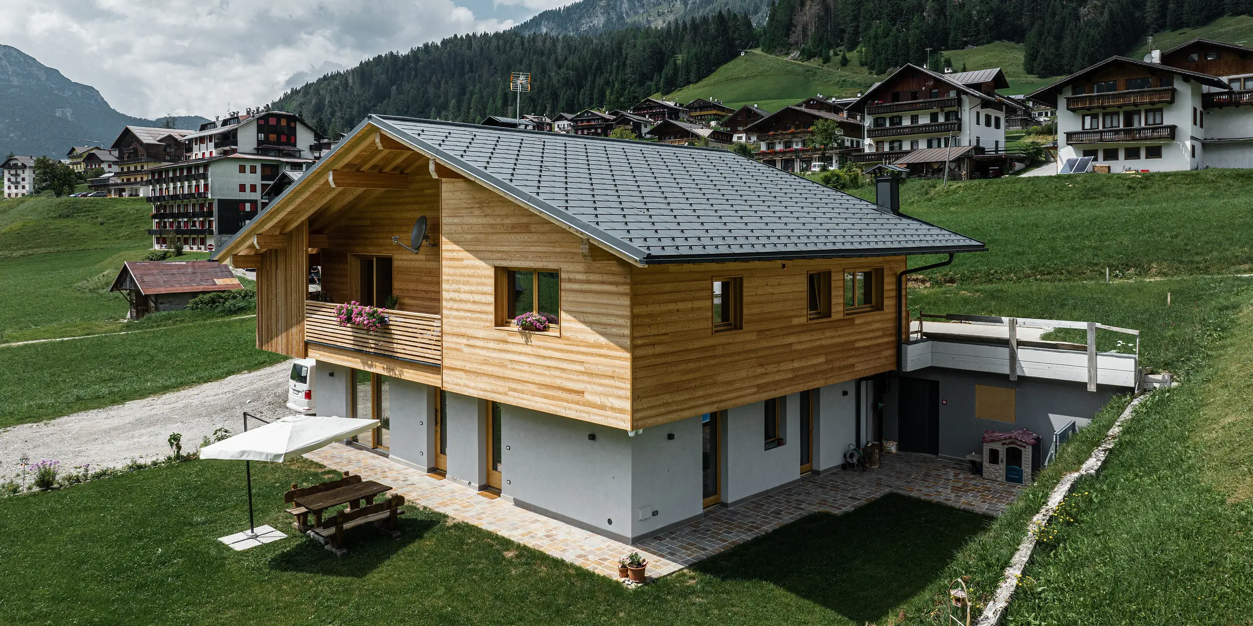 Das Einfamilienhaus Casa Hoffe in der alpinen Gemeinde Sappada, Italien, zeigt ein harmonisches Zusammenspiel von traditioneller und moderner Architektur. Ausgestattet mit PREFA Dachplatten R.16 in P.10 Schwarz, die Stabilität und Eleganz verleihen, während die Siding.X Fassadenpaneele im Eingangsbereich das Design mit einer extravaganten Note bereichern. Die langlebigen Aluminiumelemente von PREFA integrieren sich nahtlos in die für die Region typische Holzfassade und bieten dauerhaften Schutz inmitten der idyllischen Berglandschaft.