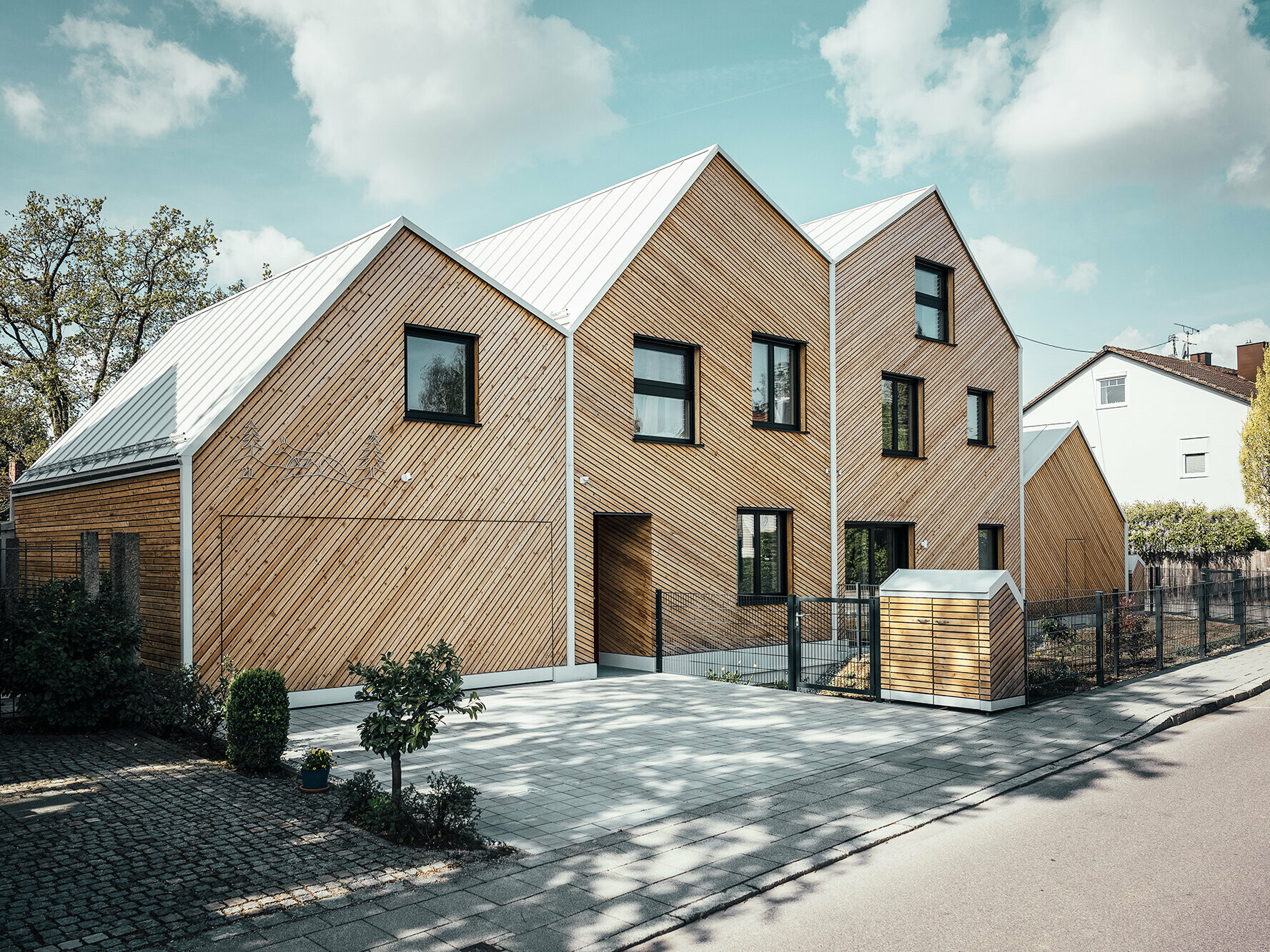 Lateral street view of Hausfuchs, view of the irregular roofscape, façade with larch wood panelling, little rubbish houses.