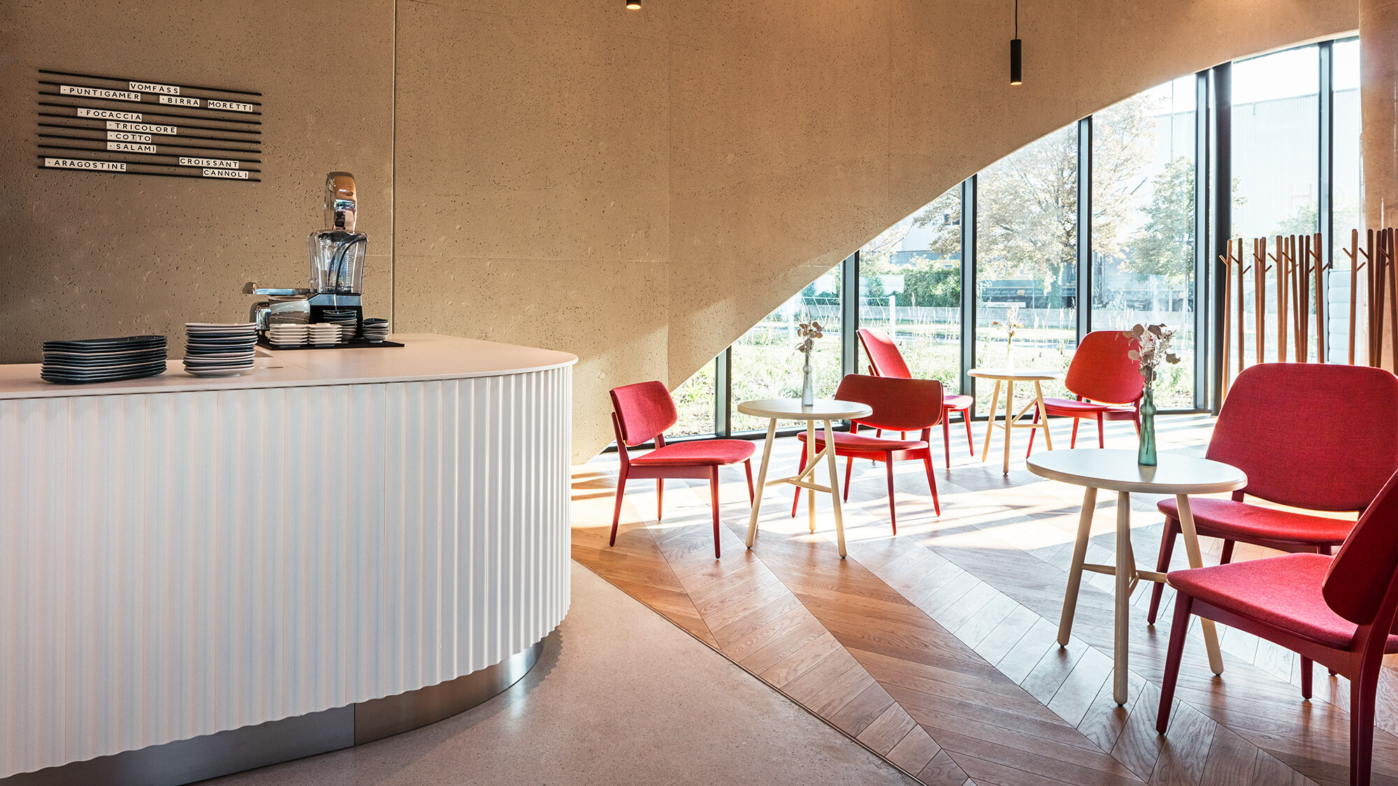 One of the restaurant's rooms with a bar, red chairs and a parquet floor; one of its round arched windows can be seen behind it.