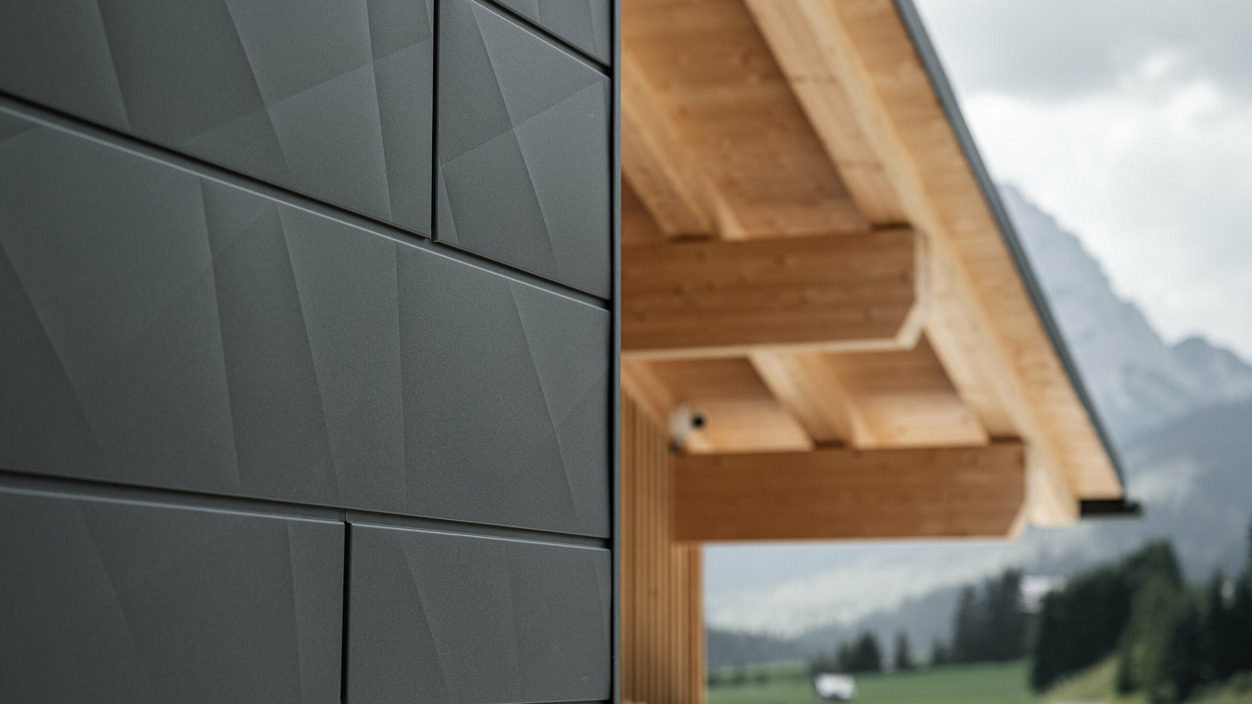 Close-up of the Siding.X façade panels in P.10 black from PREFA on Casa Hoffe in Sappada, Italy. The aluminium façade system has been skilfully installed in a modern, abstract design that forms an attractive contrast to the visible wooden elements of the roof structure. The innovative façade solution blends seamlessly into the alpine ambience and represents the combination of functionality, durability and aesthetic building culture.