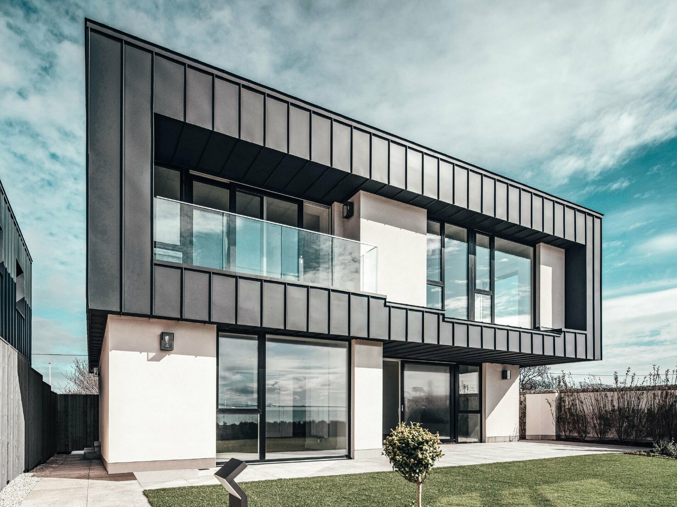 Modern terraced house with flat roof, the facade on the upper floor was designed with an angled standing seam facade made of PREFALZ in anthracite.