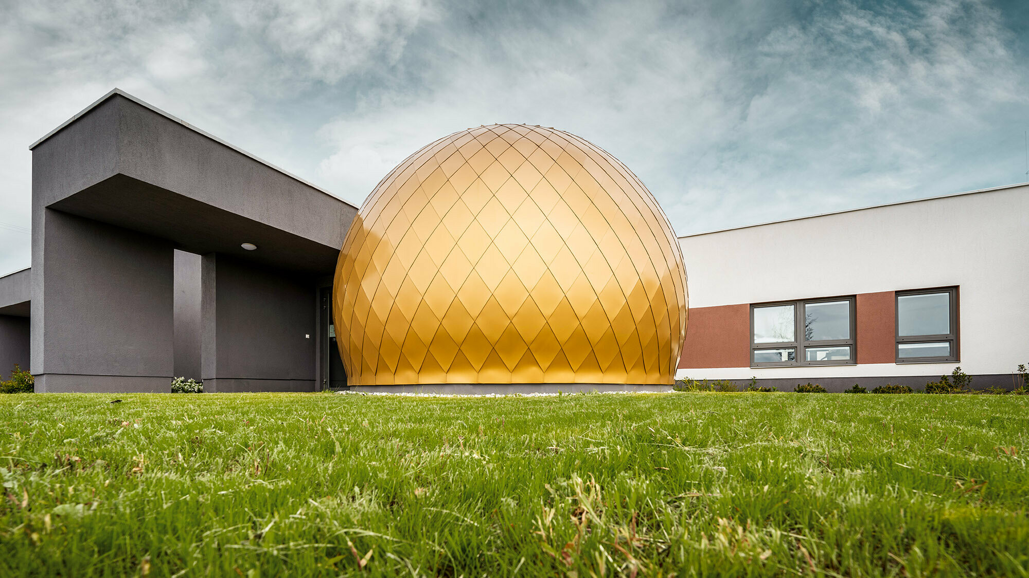 One of the round rooms from a normal perspective, the building extending behind it, the sky above it and the lawn before it.