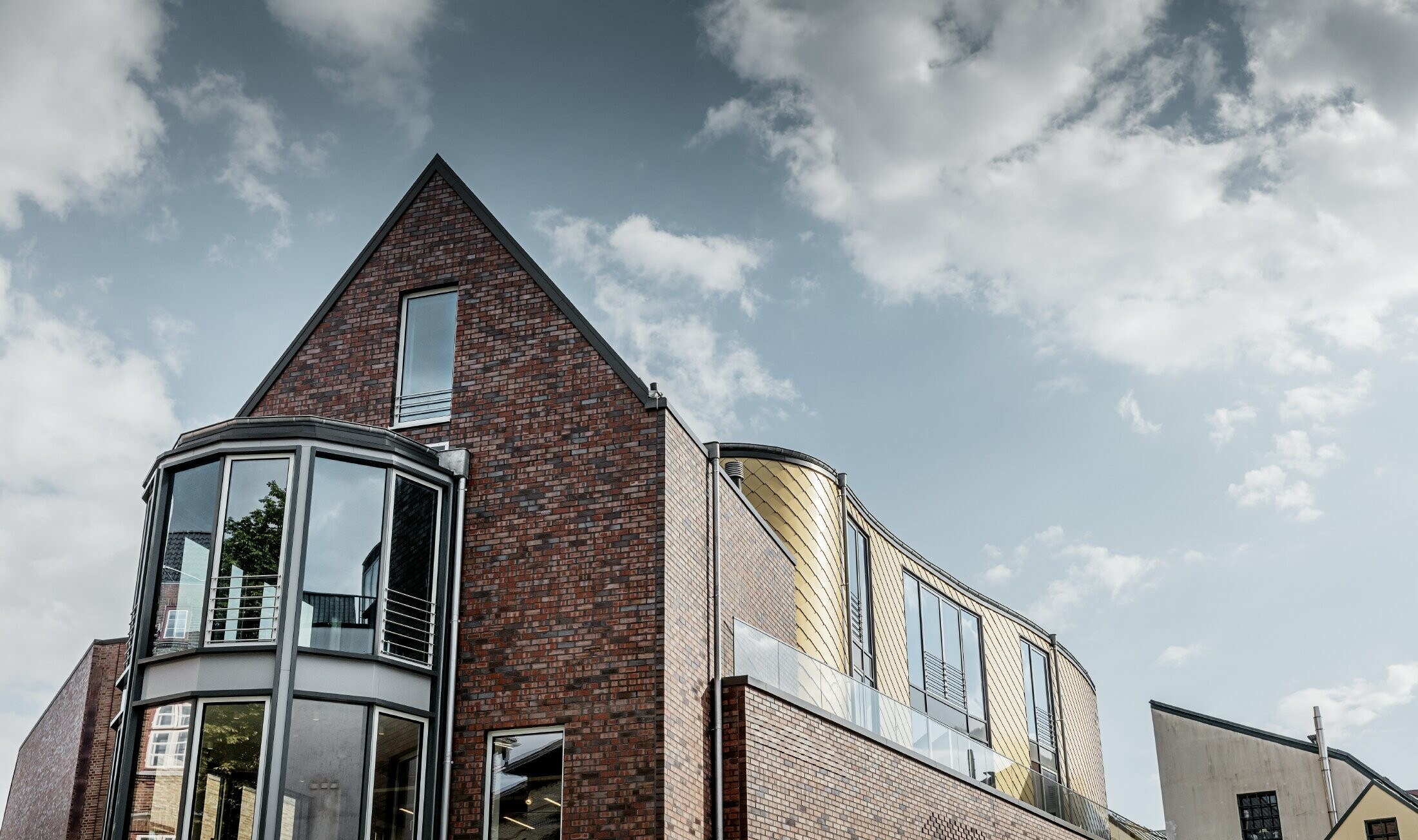 Office building with brick façade and large windows. Part of the curved façade was clad in the PREFA golden aluminium rhomboid façade tiles.