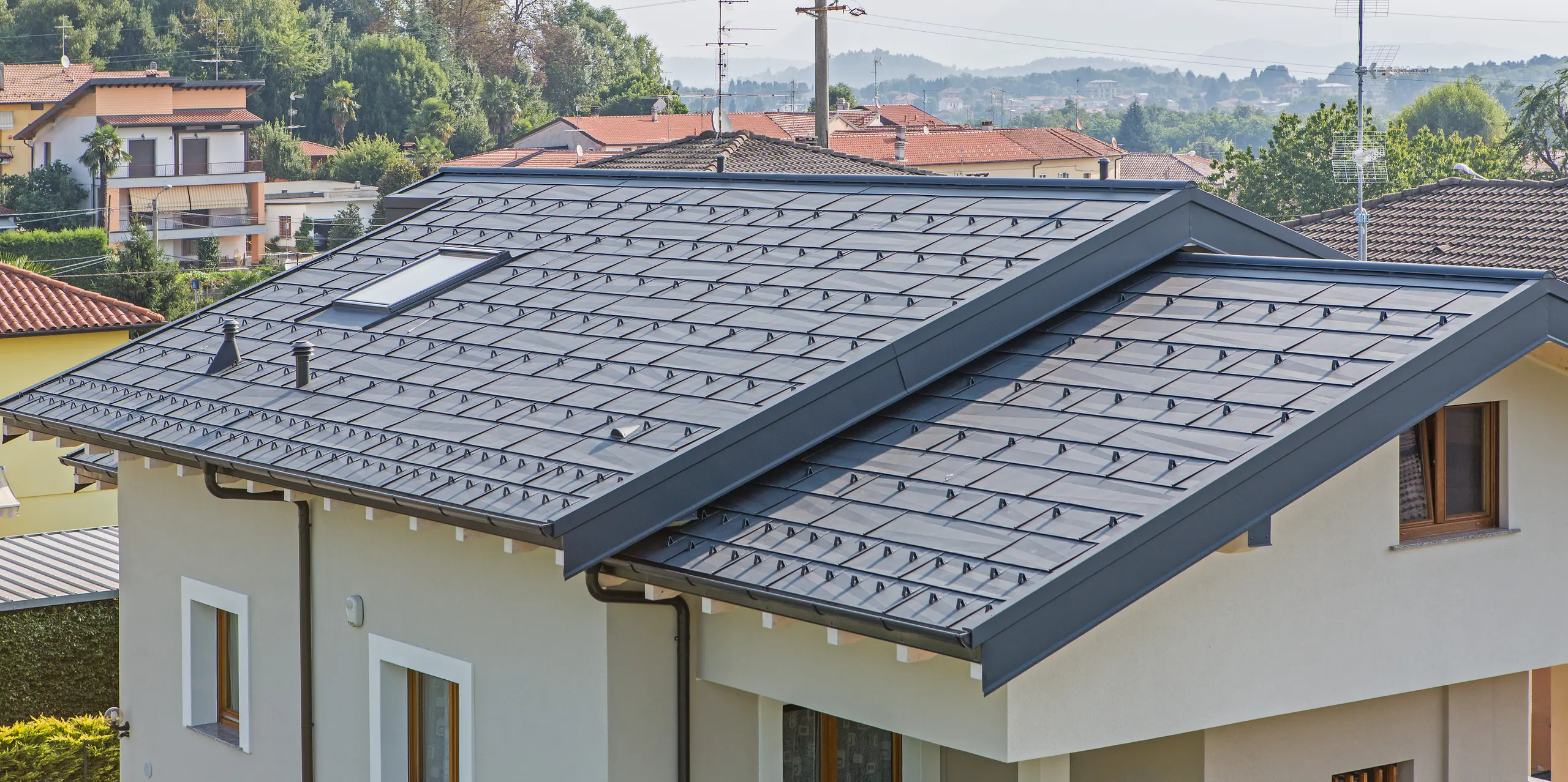 Detailaufnahme des PREFA Dachs FX.12 in P.10 Anthrazit auf einem Einfamilienhaus in Beregazzo, Italien. Die markanten, unregelmäßig gekanteten Aluminium-Dachpaneele erzeugen ein faszinierendes geometrisches Muster und ein dynamisches Lichtspiel. Die elegante Dachfläche vereint moderne Architektur mit den Vorteilen von PREFA Aluminium: langlebig, witterungsbeständig und optisch außergewöhnlich.