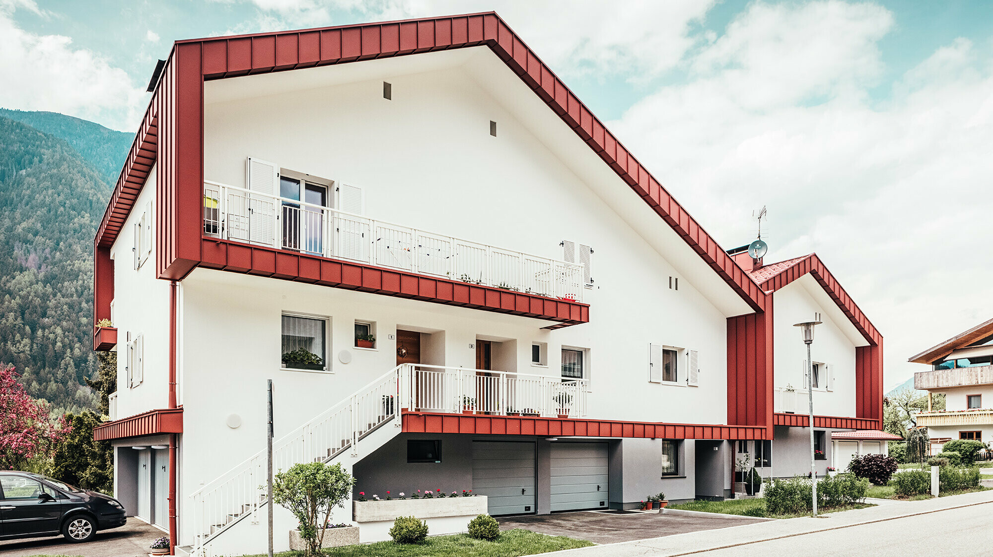After photo of the residential building in Gais: the oxide red roof panel frames the two adjoining residential buildings.