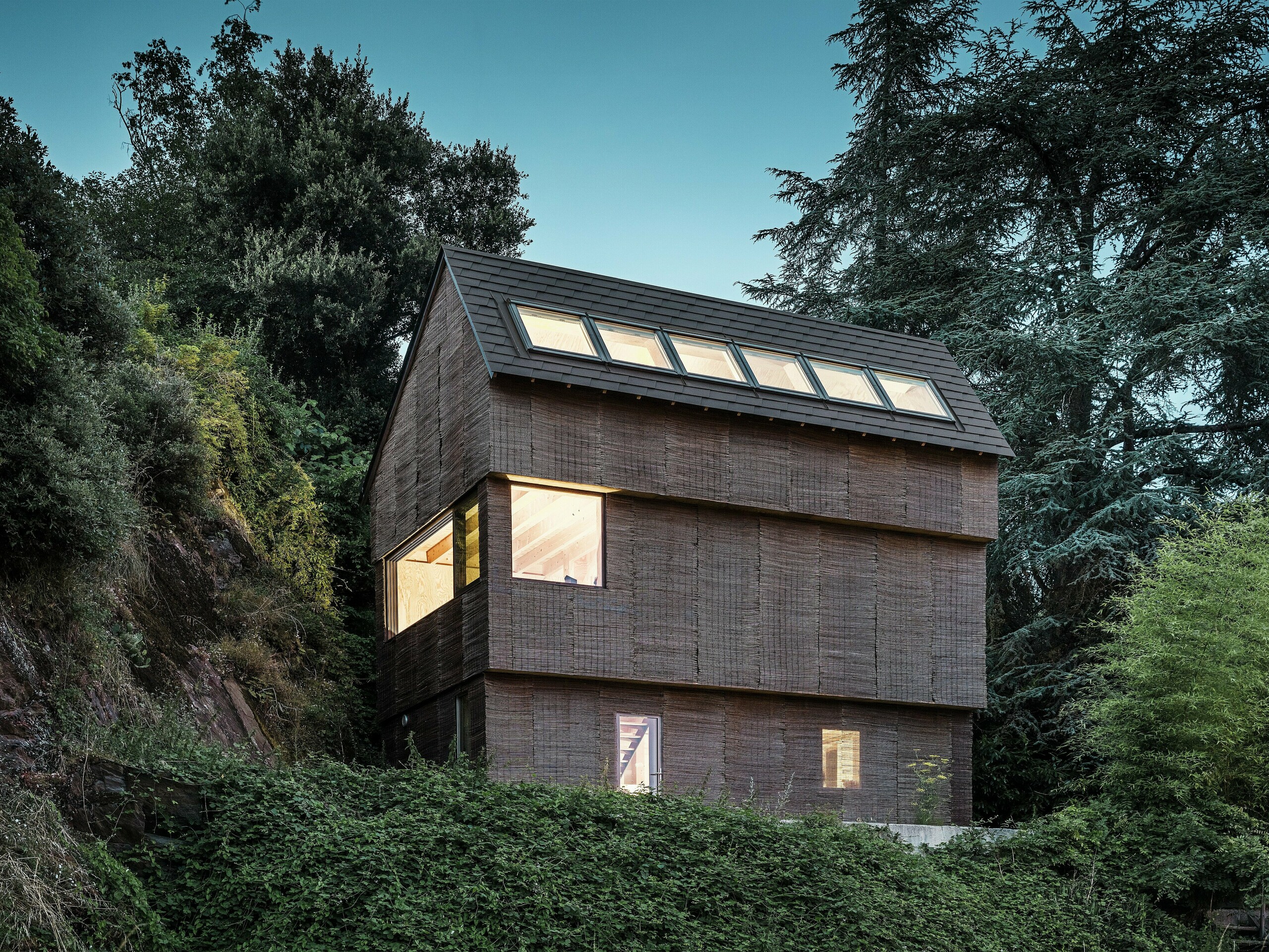 Nachtsicht eines modernen Hauses im Westen Frankreichs mit PREFA Dachschindeln in P.10 Nussbraun, großzügigen Dachfenster und nachhaltiger Weidenfassade