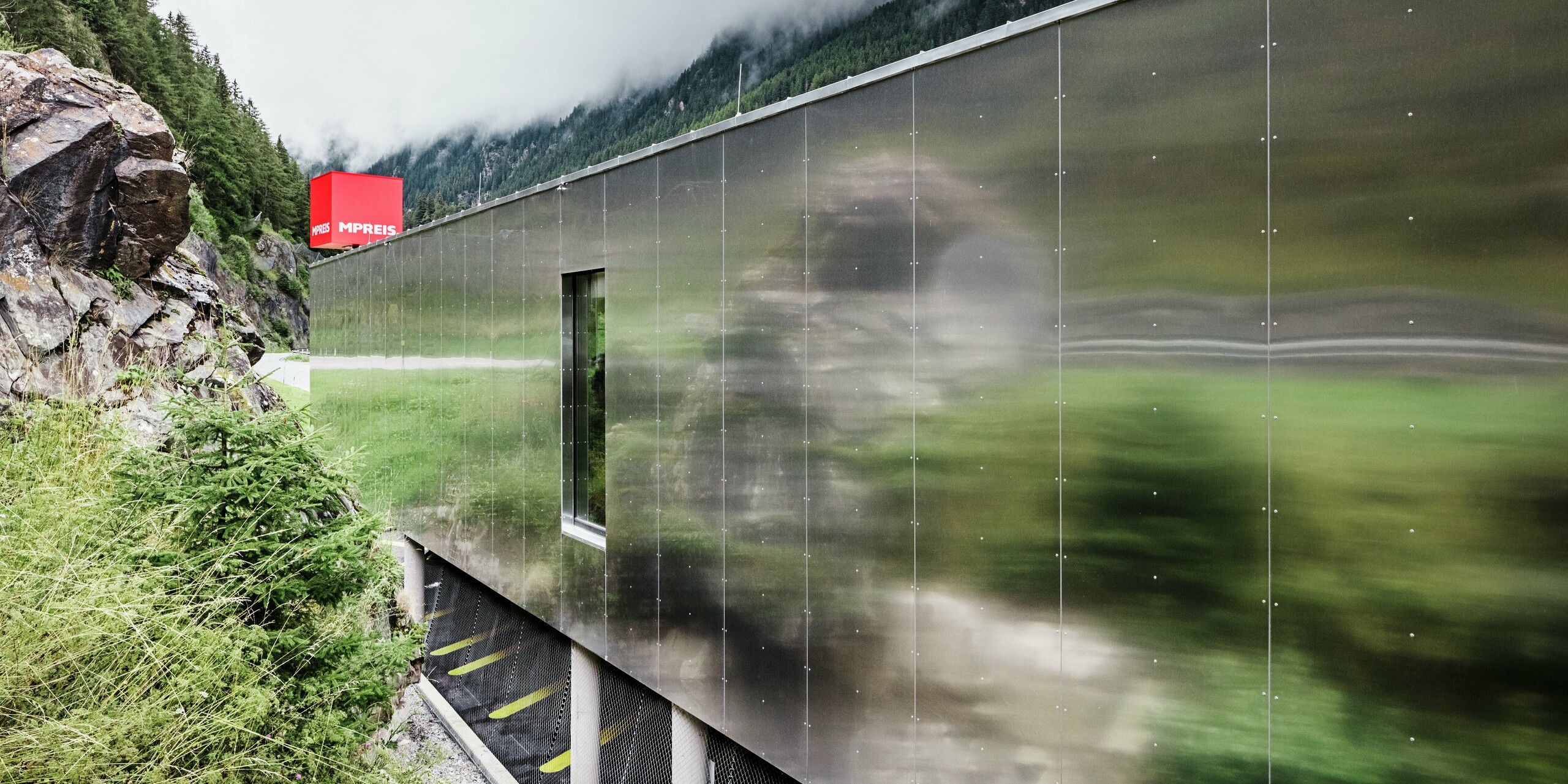 Nahaufnahme der verspiegelten Fassade des MPREIS Supermarktes in Sölden, Tirol. Die Aluminium Verbundplatten in der Sonderfarbe Reflective Natural spiegeln die umgebende Landschaft der Ötztaler Alpen wider. Die fugenlos montierten Platten erzeugen eine mattglänzende Oberfläche, die moderne Architektur mit der Natur verschmelzen lässt.