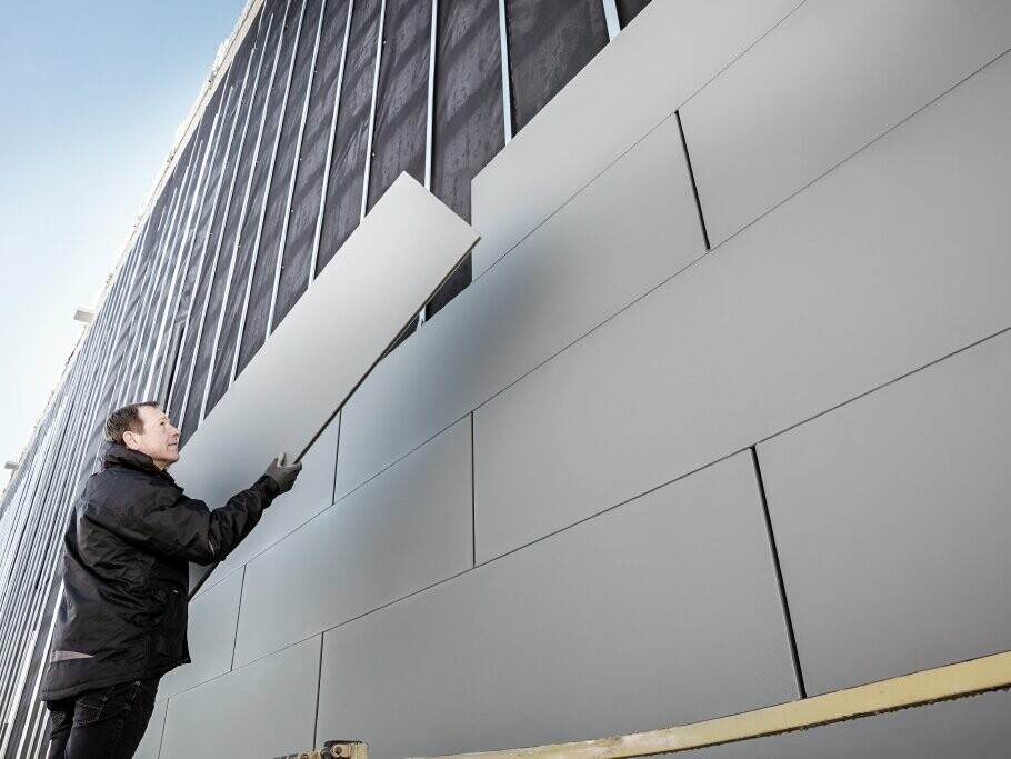 Photos of a partially completed façade clad with PREFA sidings in the 500 width. The roofer is installing another façade panel. The image is taken from below. 