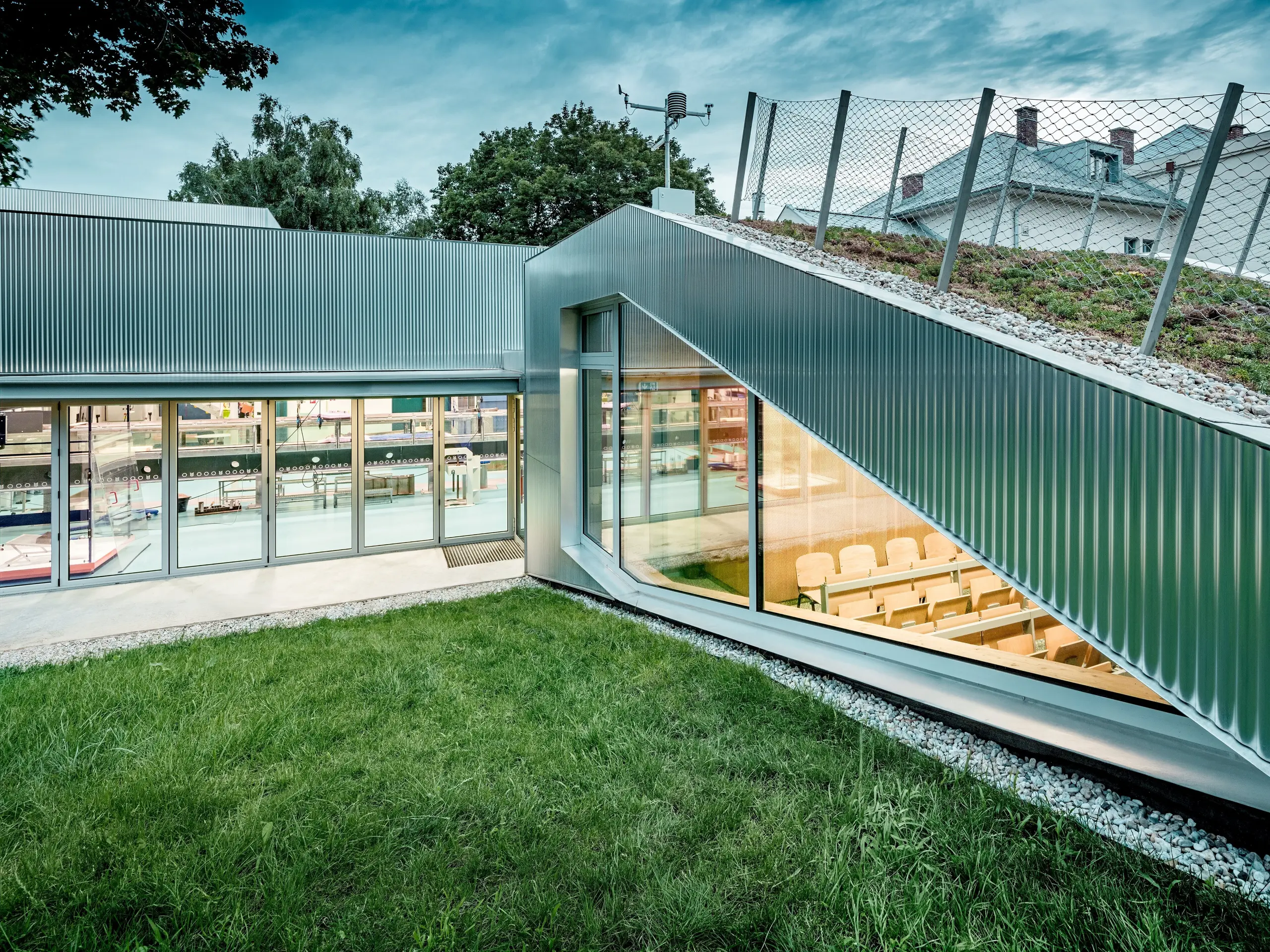 Das Envirocenter Nitra beeindruckt mit seiner silbern schimmernden PREFA Aluminiumfassade aus Strangpressprofil Welle in Naturblank. Die markante Wellenstruktur umrahmt eine großzügige, dreieckige Glasfront mit Blick in den lichtdurchfluteten Vortragssaal. Das begrünte Schrägdach verbindet Architektur und Natur, während die langlebigen, witterungsbeständigen Aluminiumprofile moderne Ästhetik und Funktionalität vereinen.
