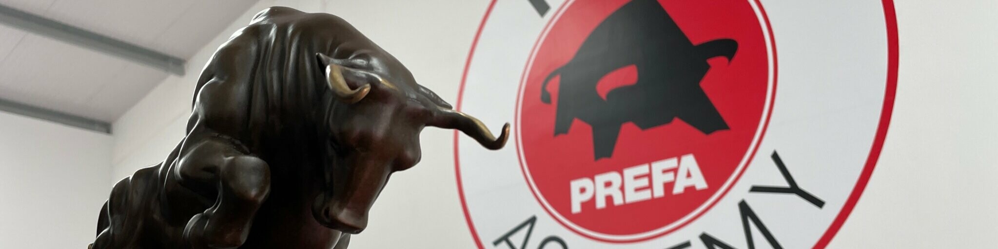 Photo of a bull as a statue. The logo of the PREFA Academy in the UK can be seen in the background.