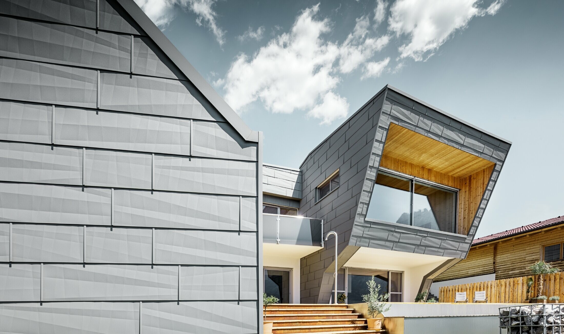 Light grey façade of a detached house in Lienz clad in the PREFA FX.12 façade panel in P.10 light grey in combination with a wooden façade.