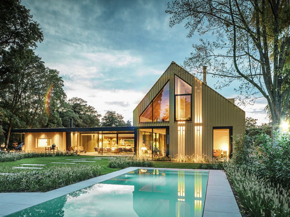 View of the detached house in Elst covered in Prefalz and Falzonal. The house is surrounded by trees and a pool can be seen in the foreground.