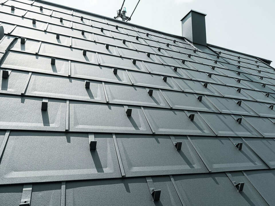 Detailed view of the PREFA R.16 roof tile in colour P.10 anthracite. PREFA snow guards and a smoke hood can be seen on the roof.