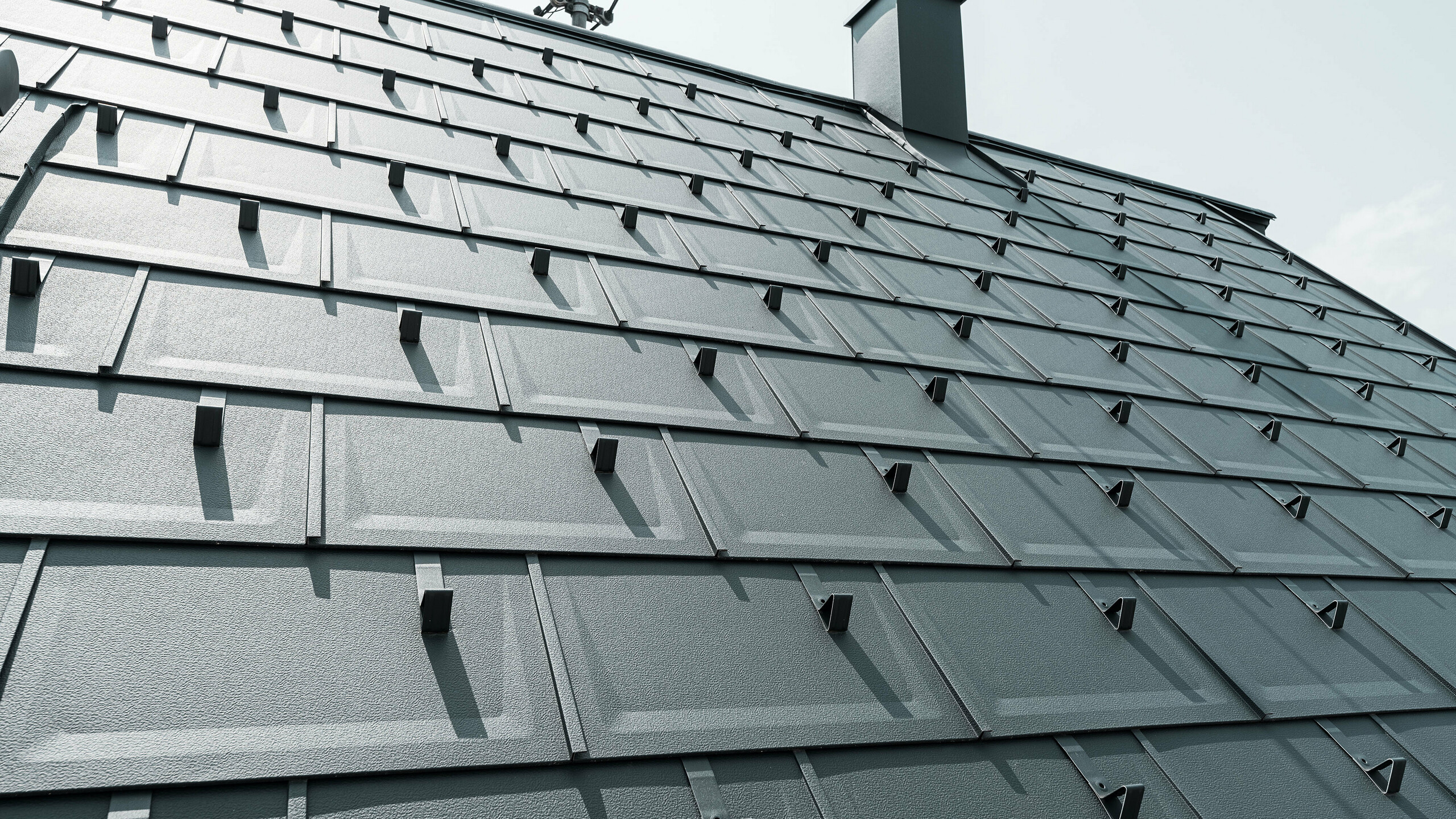 Detailed view of the PREFA R.16 roof tile in colour P.10 anthracite. PREFA snow guards and a smoke hood can be seen on the roof.