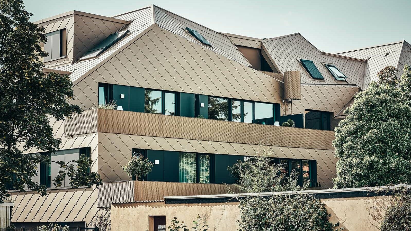 The rhomboid-shaped 44 × 44 façade tile in the special P.10 Bronze coating stretches over the entire structure like a uniform skin and gives the surface a pearly quality.