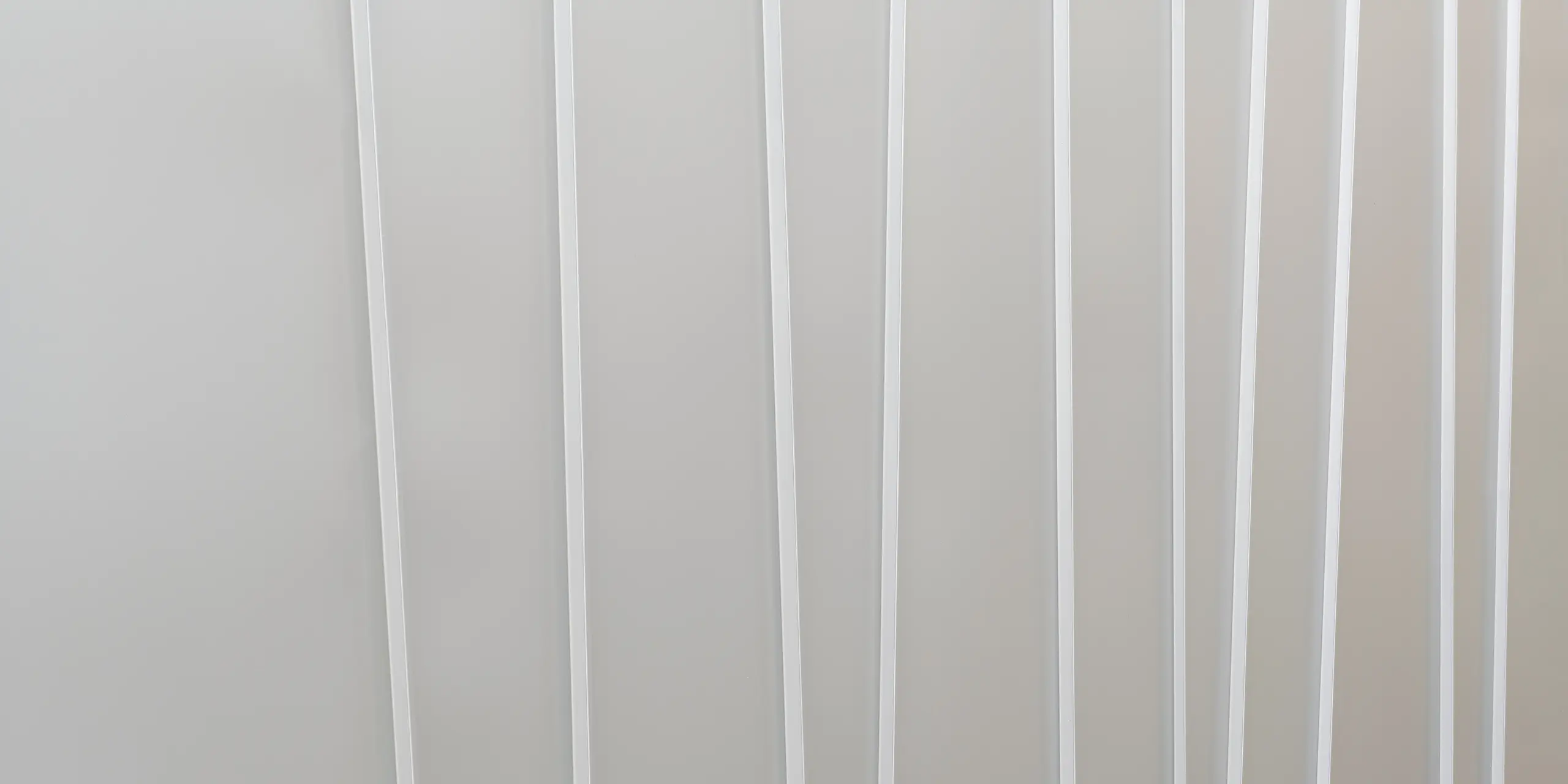 Nahaufnahme eines modernen Fassadensystems aus PREFALZ in Hellgrau mit verschiedenen Scharenbreiten. Die klare und minimalistische Textur vermittelt ein Gefühl von Ordnung und zeitgemäßem Design.