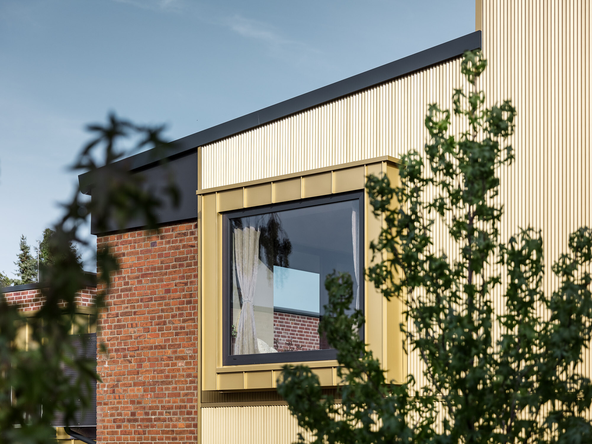 A close-up of one of the buildings with a brick façade, the PREFA façade with a profile and a window framed with Falzonal.