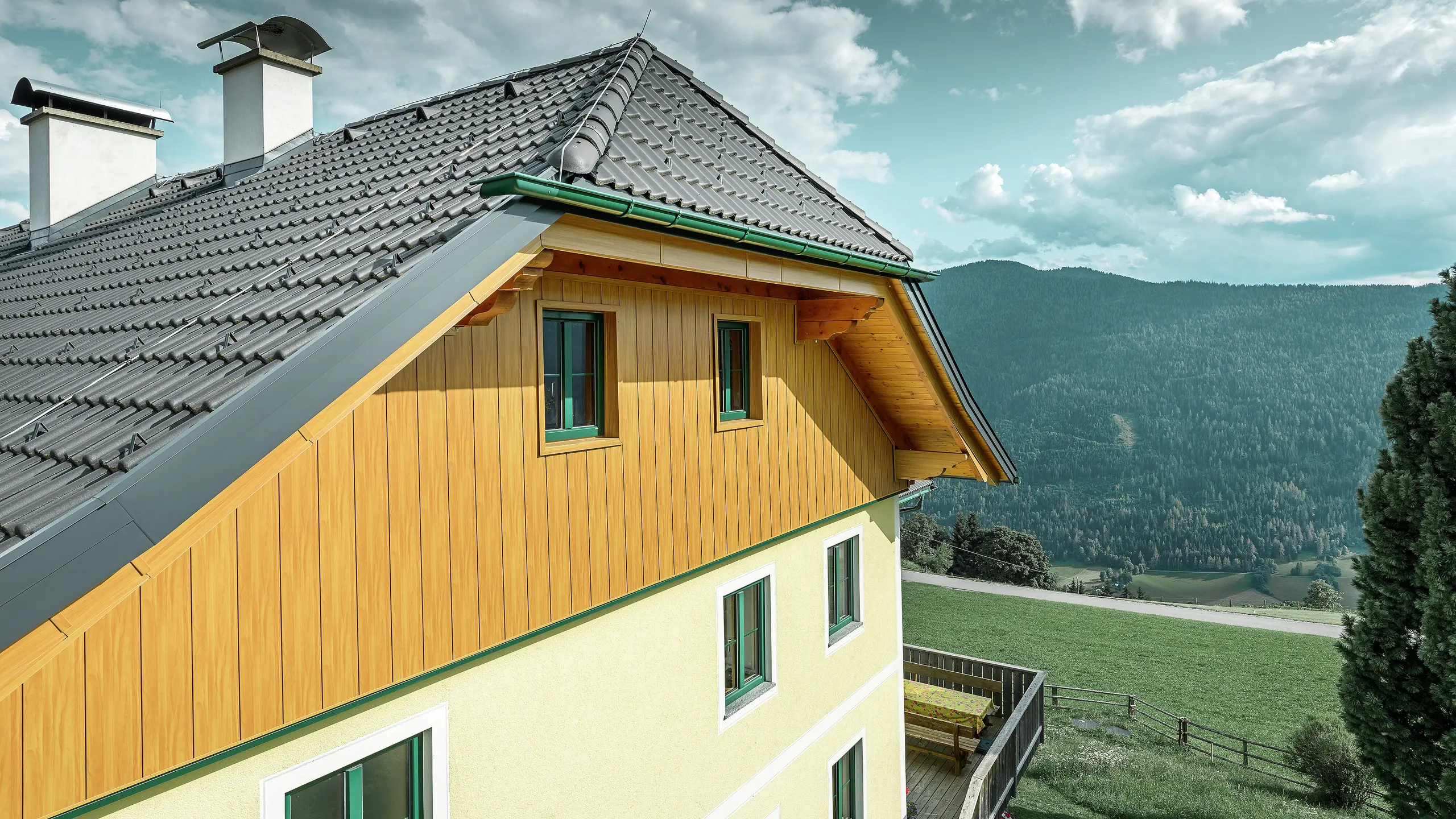 Detailansicht der Giebelverkleidung mit PREFA Sidings in Eiche natur an einem Wohnhaus in Ranten mit Blick auf die umliegende Berglandschaft.
