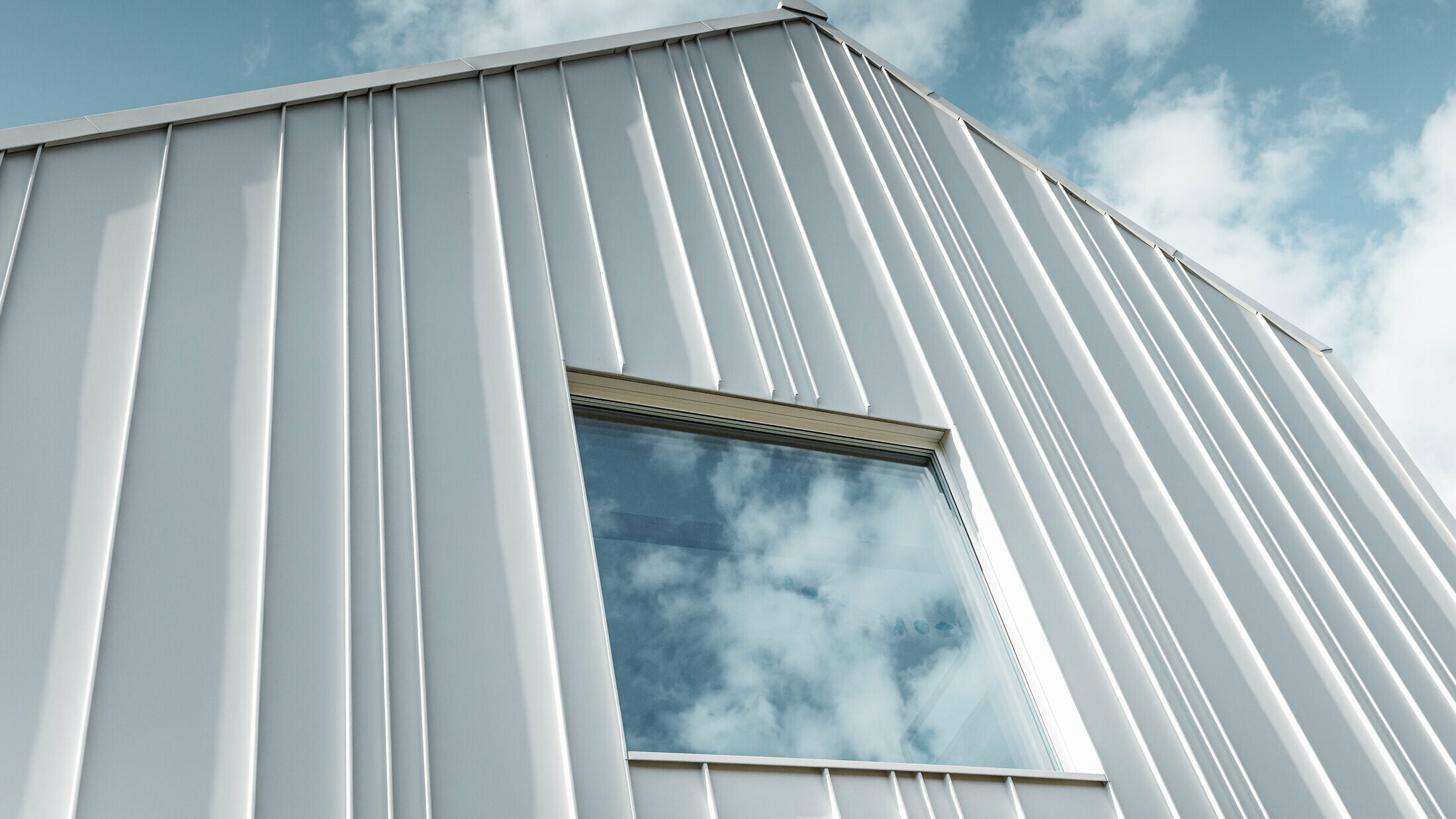 white PREFALZ as angled standing seam on the façade with different panel widths and a window