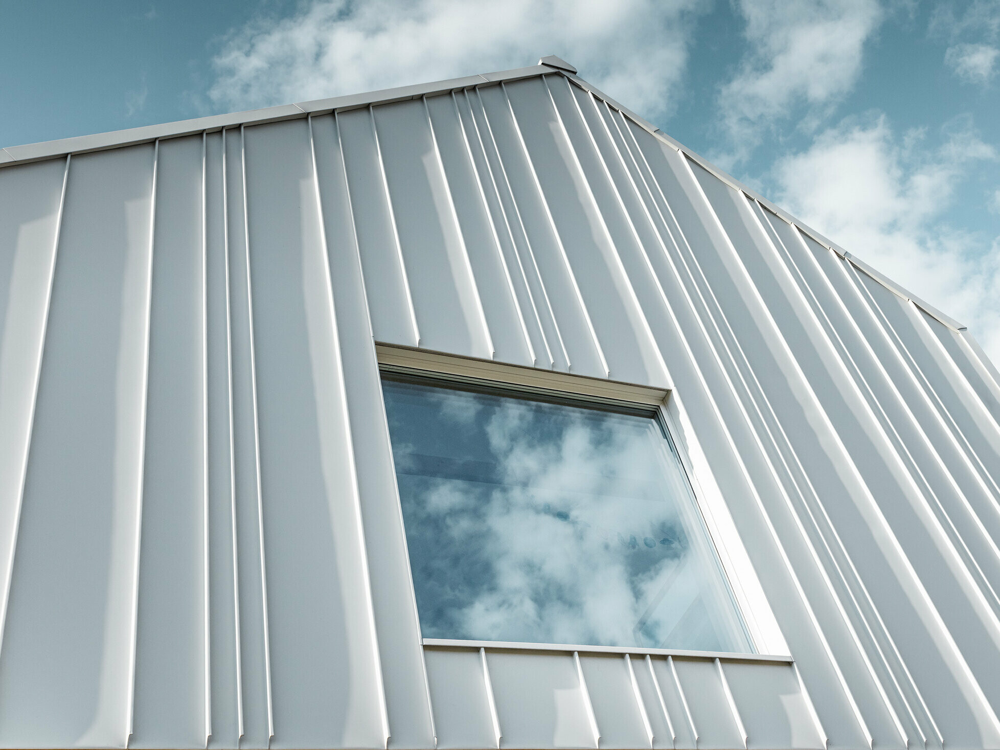 white PREFALZ as angled standing seam on the façade with different panel widths and a window